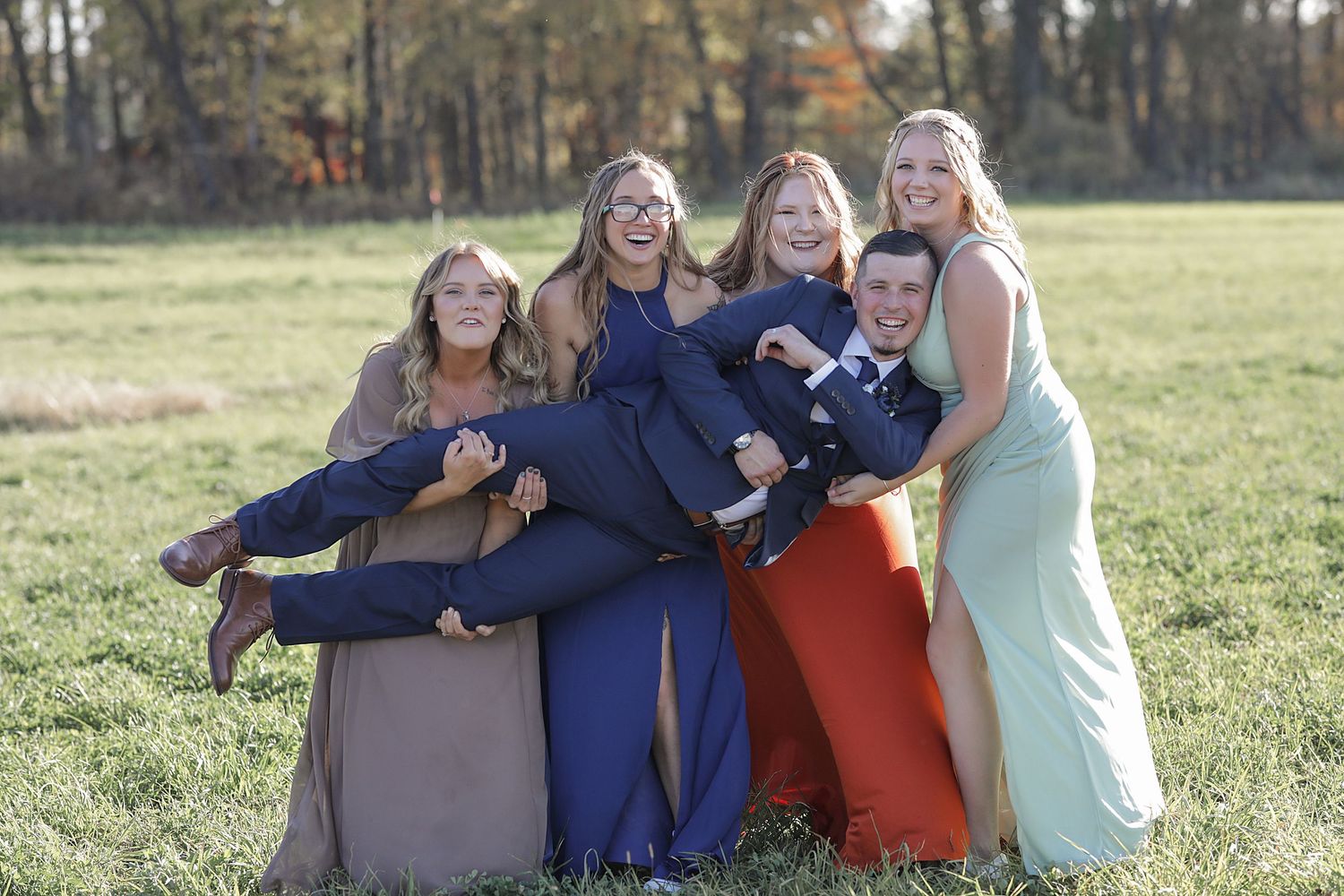 Wedding party posing playfully in an autumn field wearing coordinated colors of navy, orange, and mint.