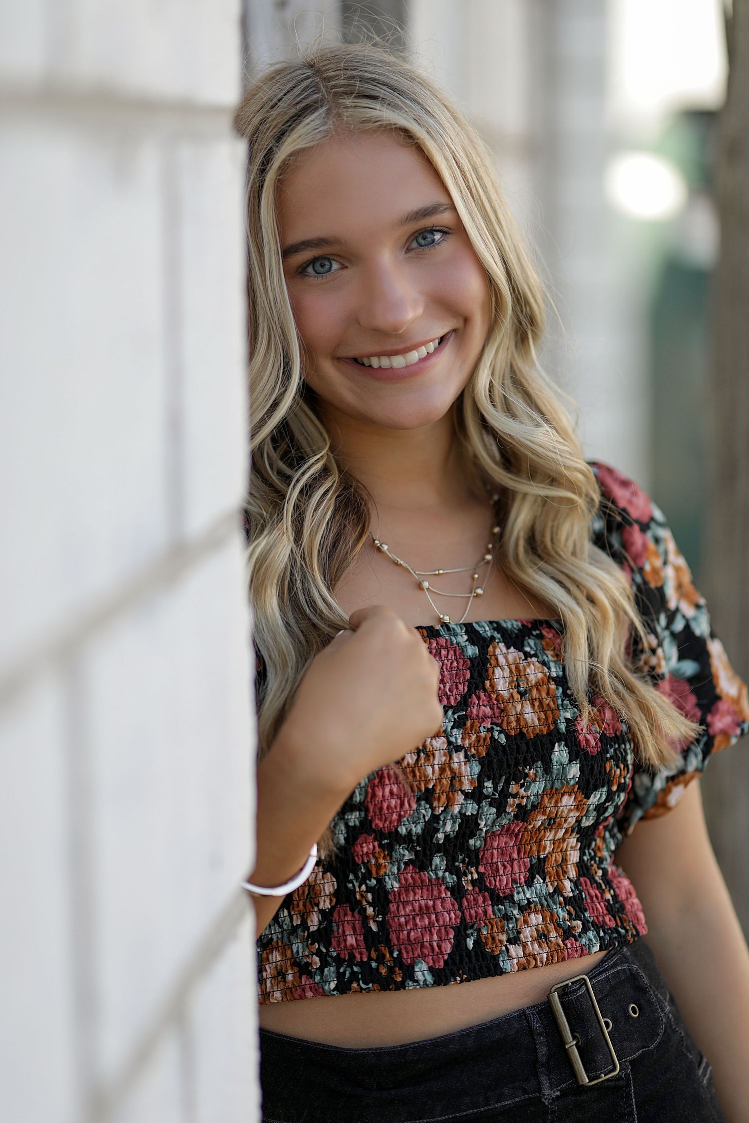 Portrait with flowing blonde waves wearing a floral smocked crop top and dark pants in natural lighting.