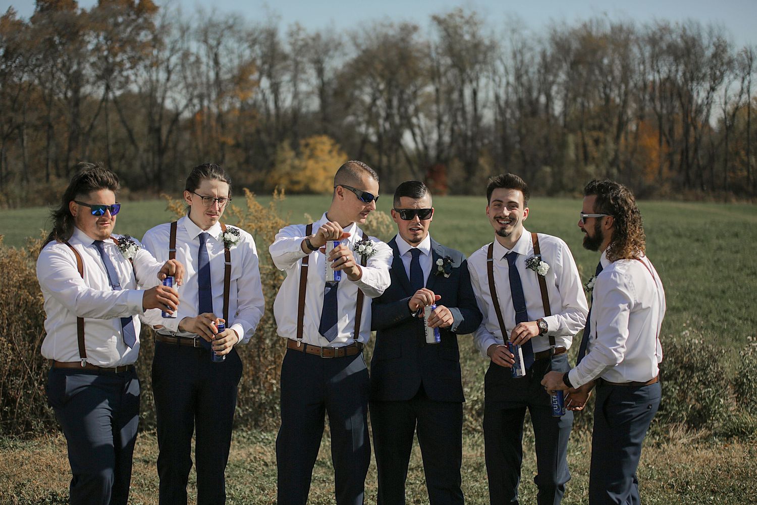 Groomsmen in white shirts and suspenders lined up outdoors for wedding photos.