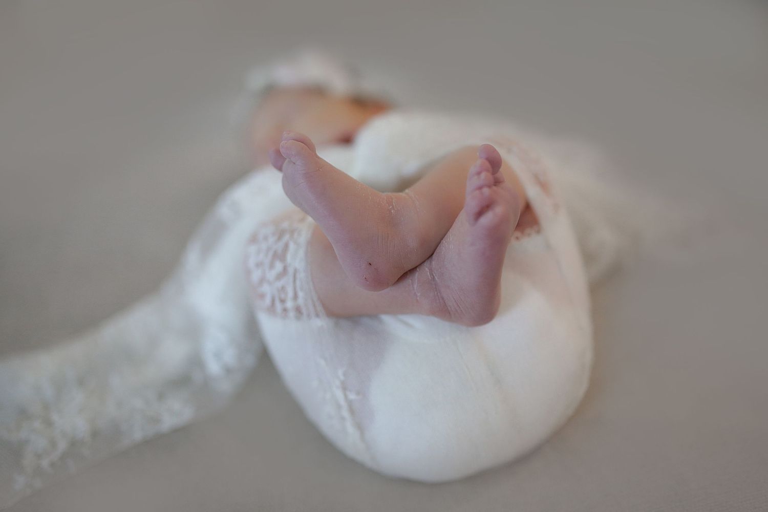 Tiny newborn baby feet peeking out from soft white lace blanket in a dreamy close up photograph.