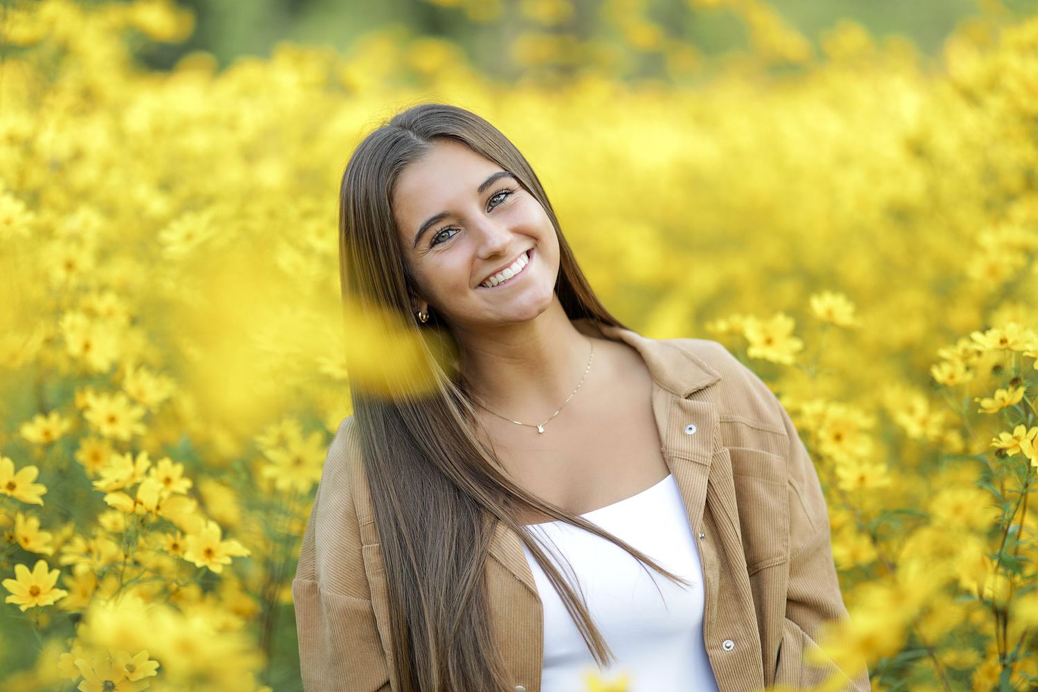 Someone poses joyfully in a field of vibrant yellow canola flowers on a bright sunny day.