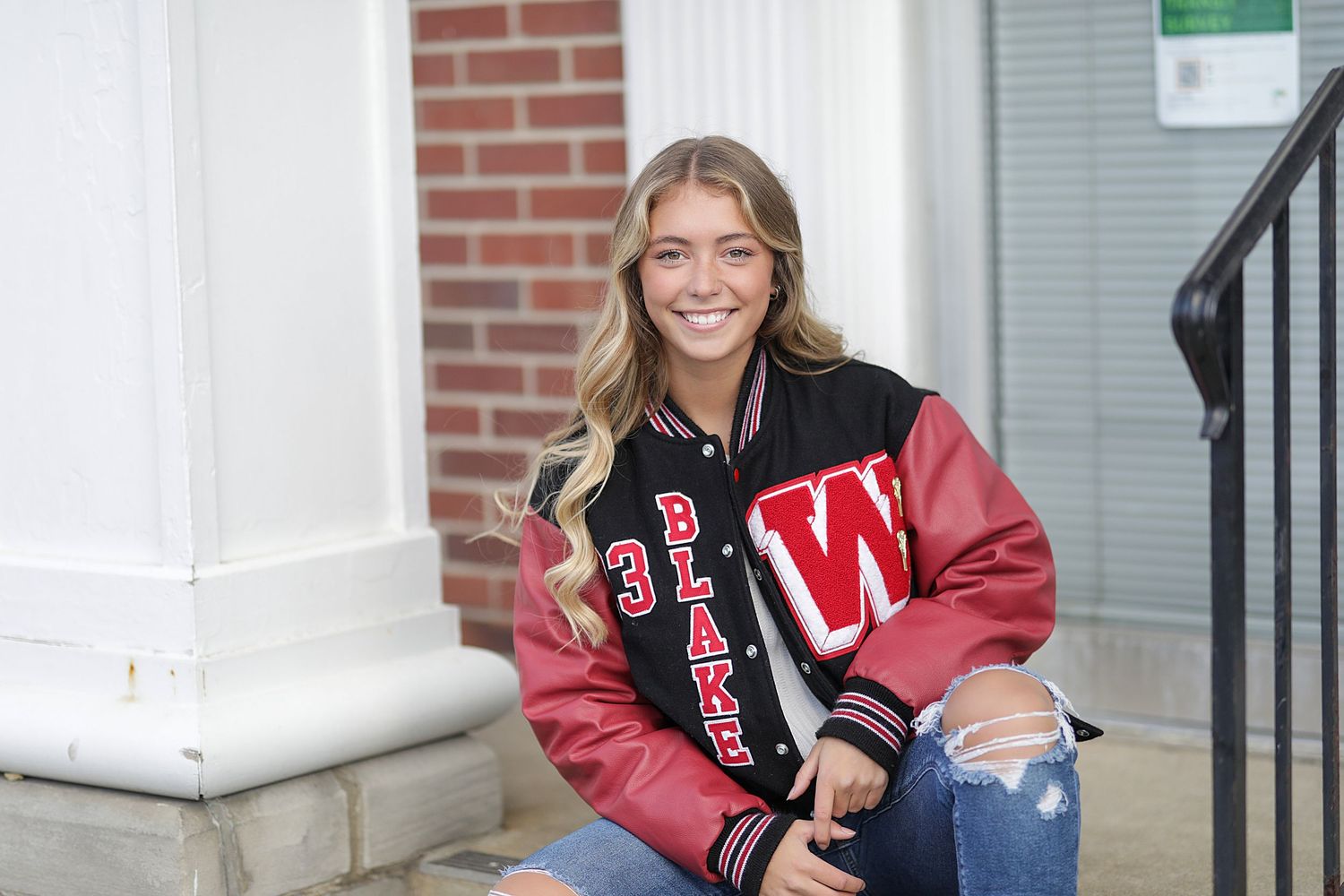Students in varsity jackets gather on the steps of a brick building with white columns at what appears to be a campus entrance.