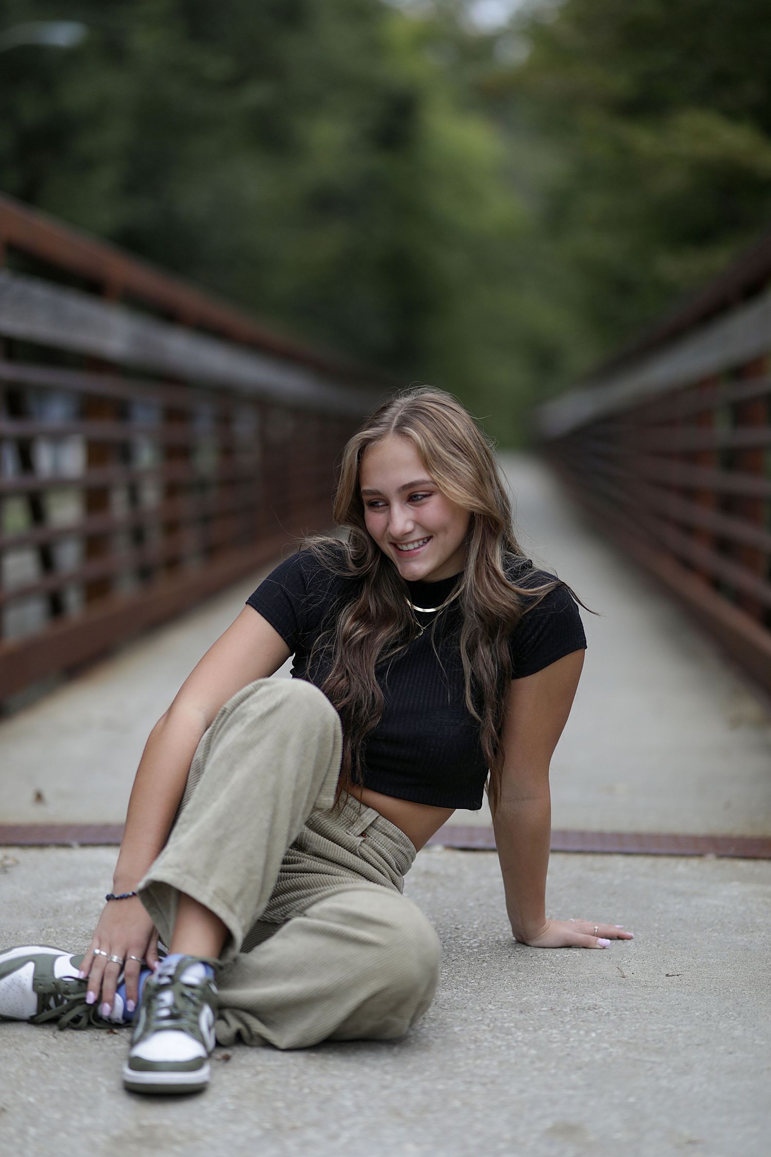 Fashion model in casual wear sitting on wooden bridge wearing crop top and cargo pants with metallic sneakers.