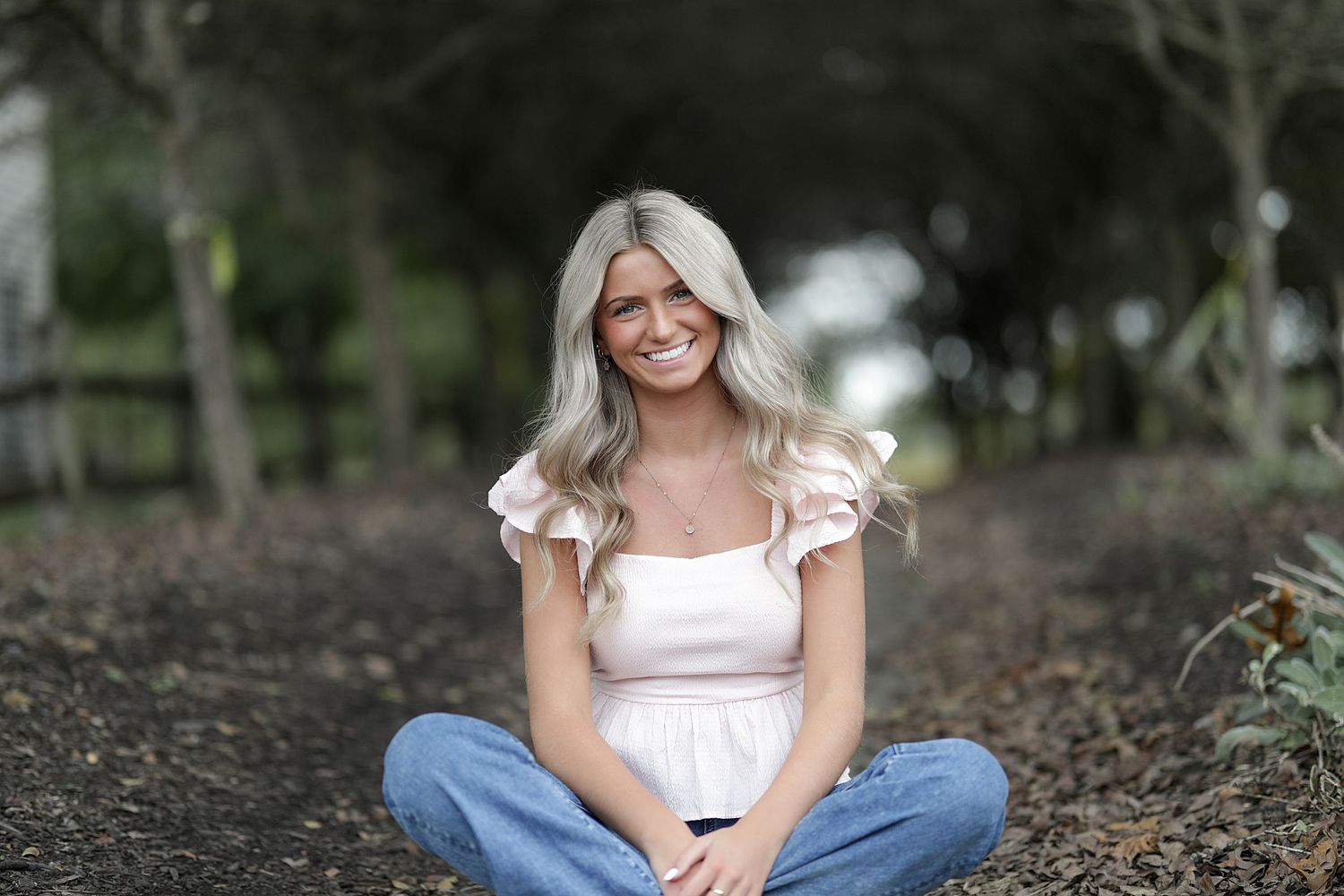 Woman in white dress sitting on autumn leaves in park for casual outdoor portrait photography session.