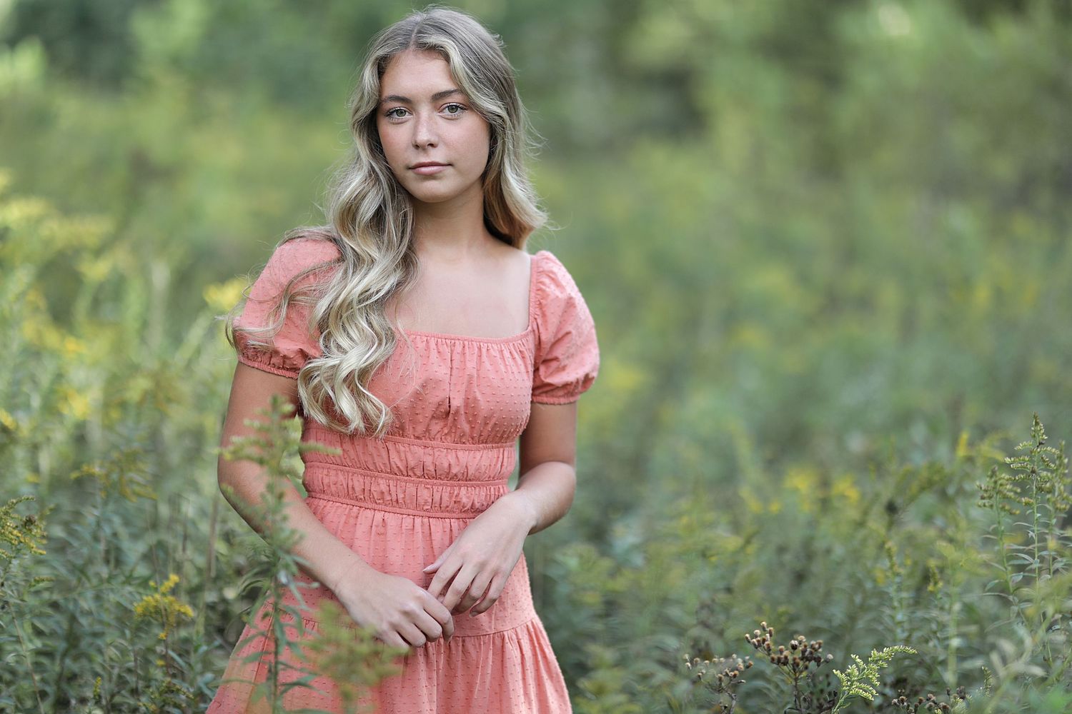 Soft peach ruffled dress worn by a woman standing in a lush green meadow of wildflowers.
