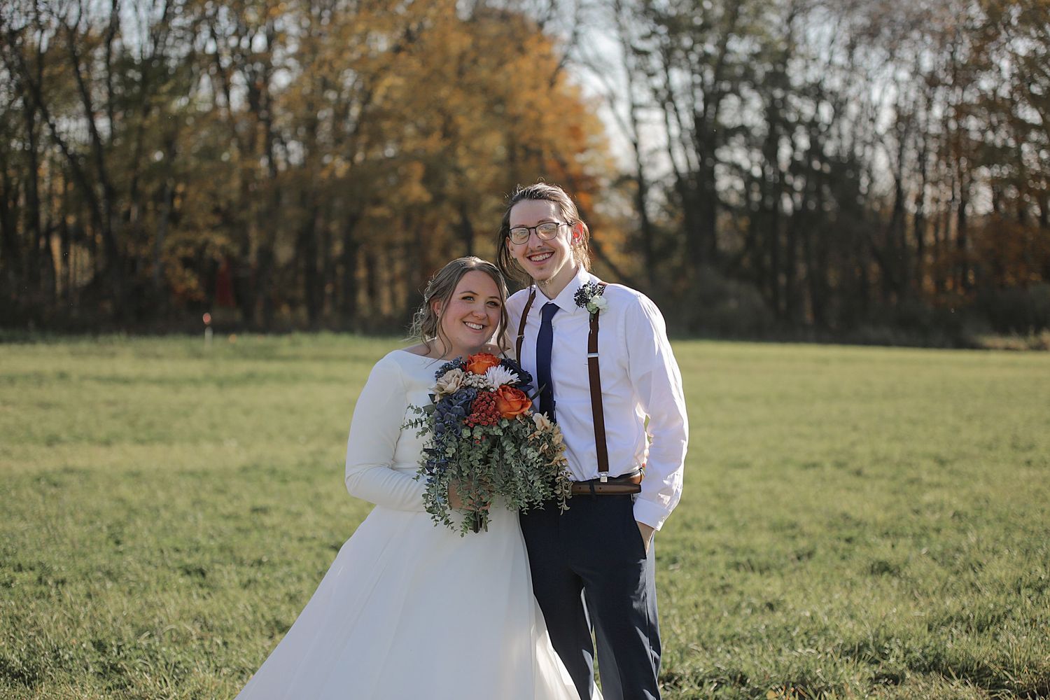 A wedding couple shares a candid moment in a field during golden hour.