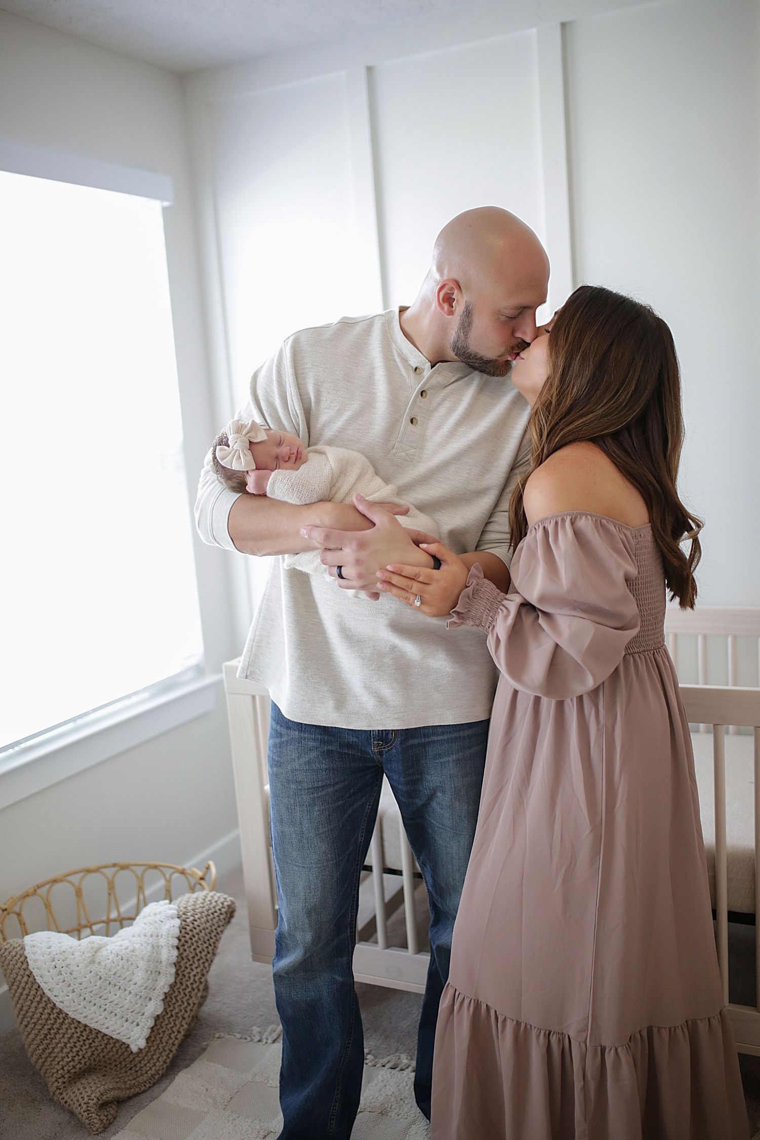 A couple shares an intimate moment dancing together in a bright sun-lit room with white walls and rattan furniture.