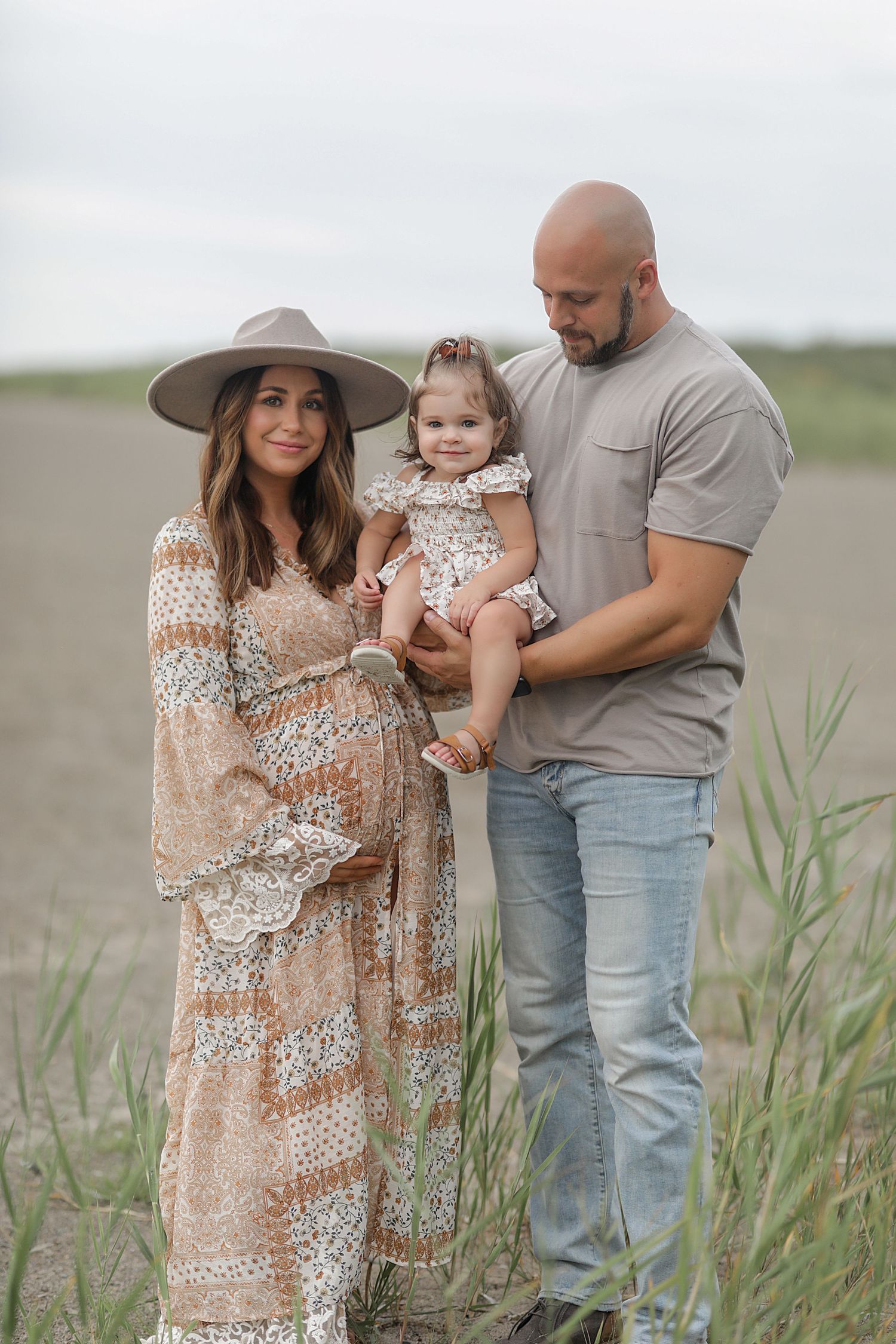 Family shares tender moments together while standing in tall grass on a cloudy day at the beach.