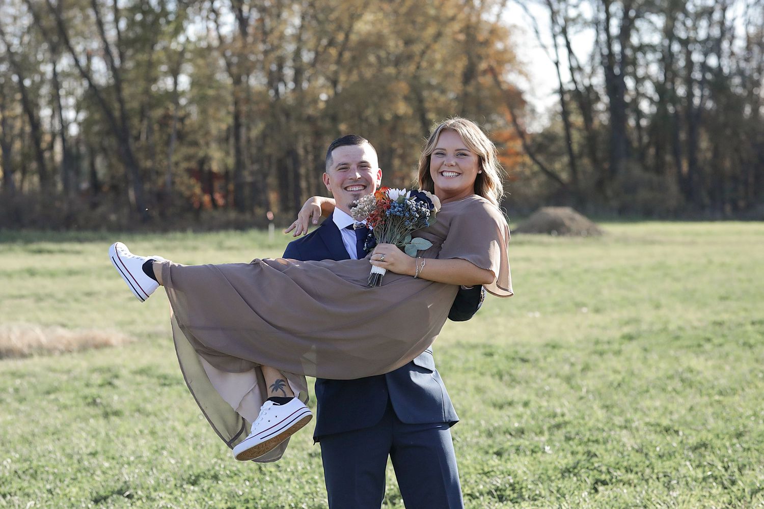 Playful moment captured during outdoor wedding photoshoot in autumn field.