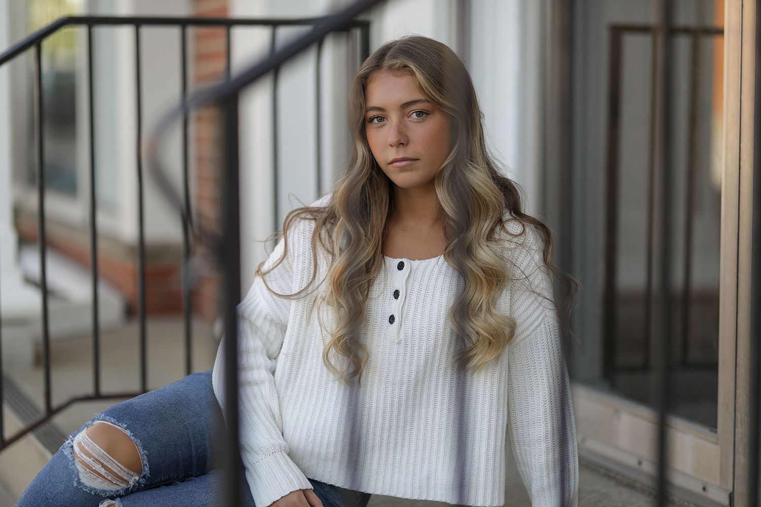 Woman in winter sweater and jeans stands by railing in natural light setting.