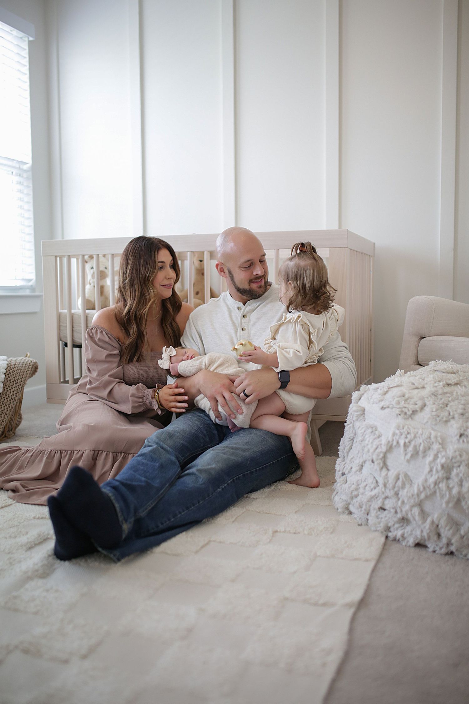 Family sitting together on comfortable white bedding in bright bedroom with natural light streaming through window.