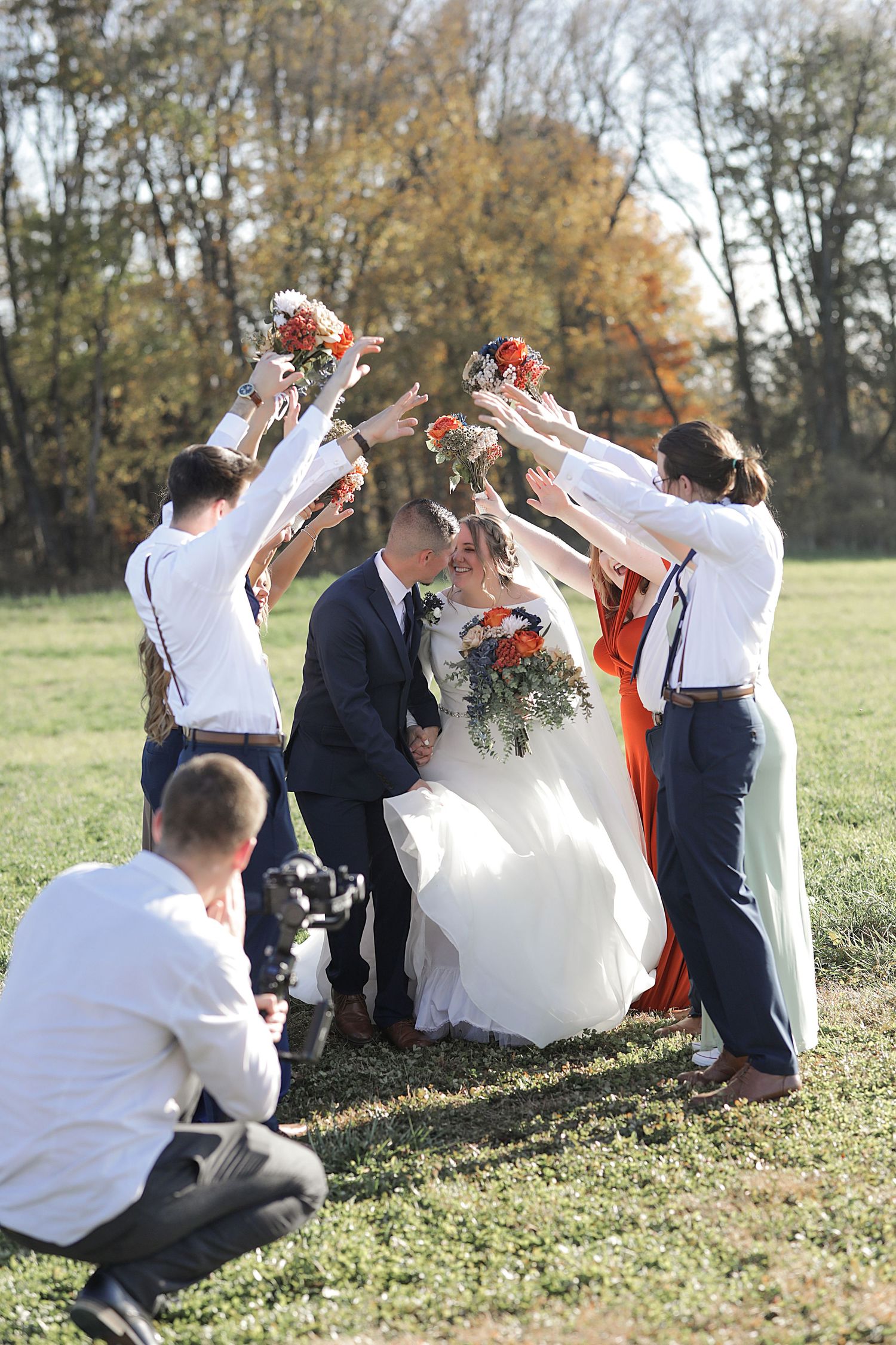 Wedding party throws celebratory flower petals over newlyweds during outdoor autumn ceremony.
