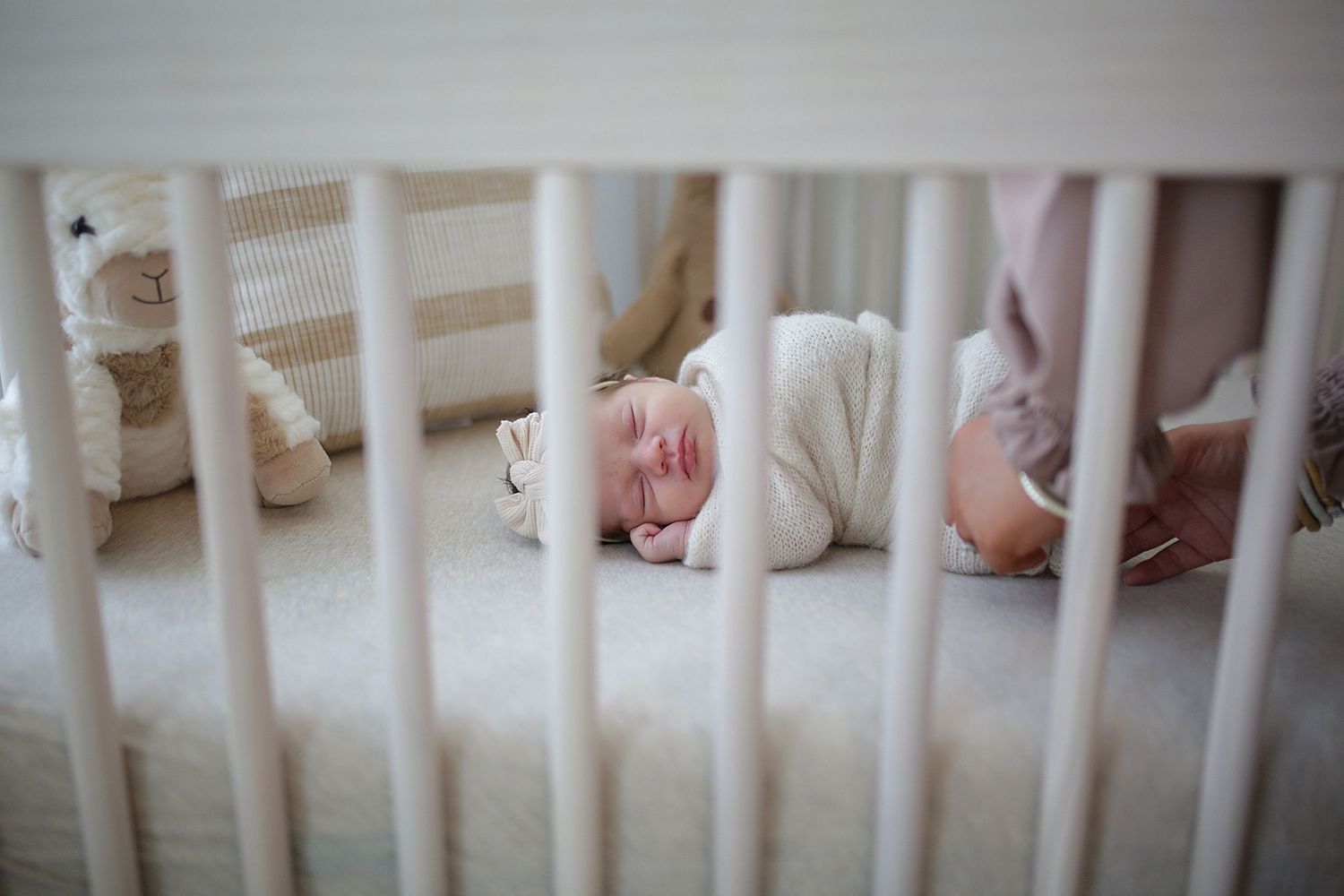A small infant sleeping peacefully in a white wooden crib with soft bedding.