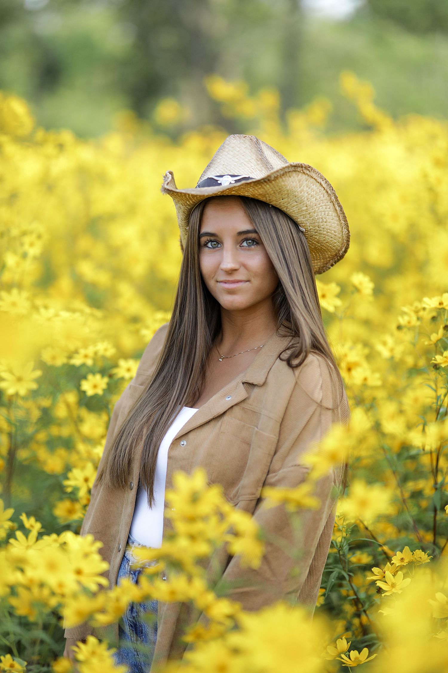 Artistic portrait in a meadow of yellow wildflowers with someone wearing a cowboy hat and tan jacket.