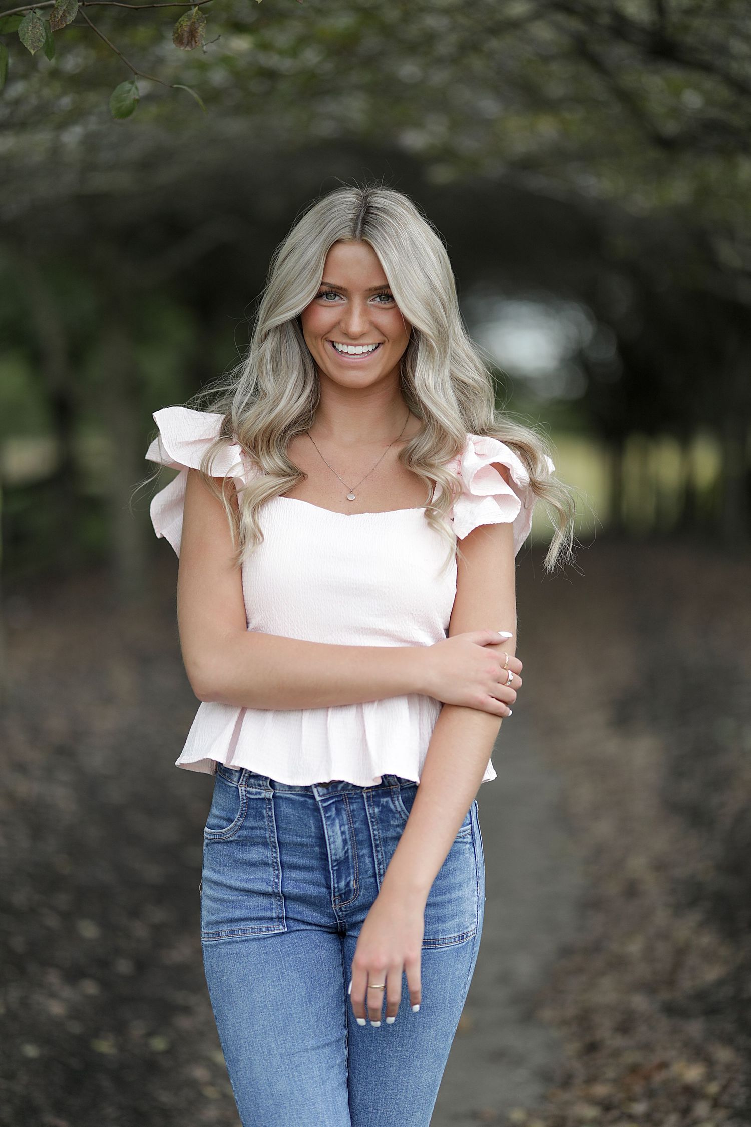 A white ruffle sleeve top paired with classic blue jeans creates a casual summer outfit against a blurred natural background.