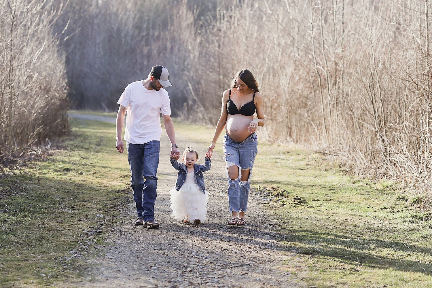 A couple and a small child walk down a wooded trail holding hands during a sunset outdoor family photo session.