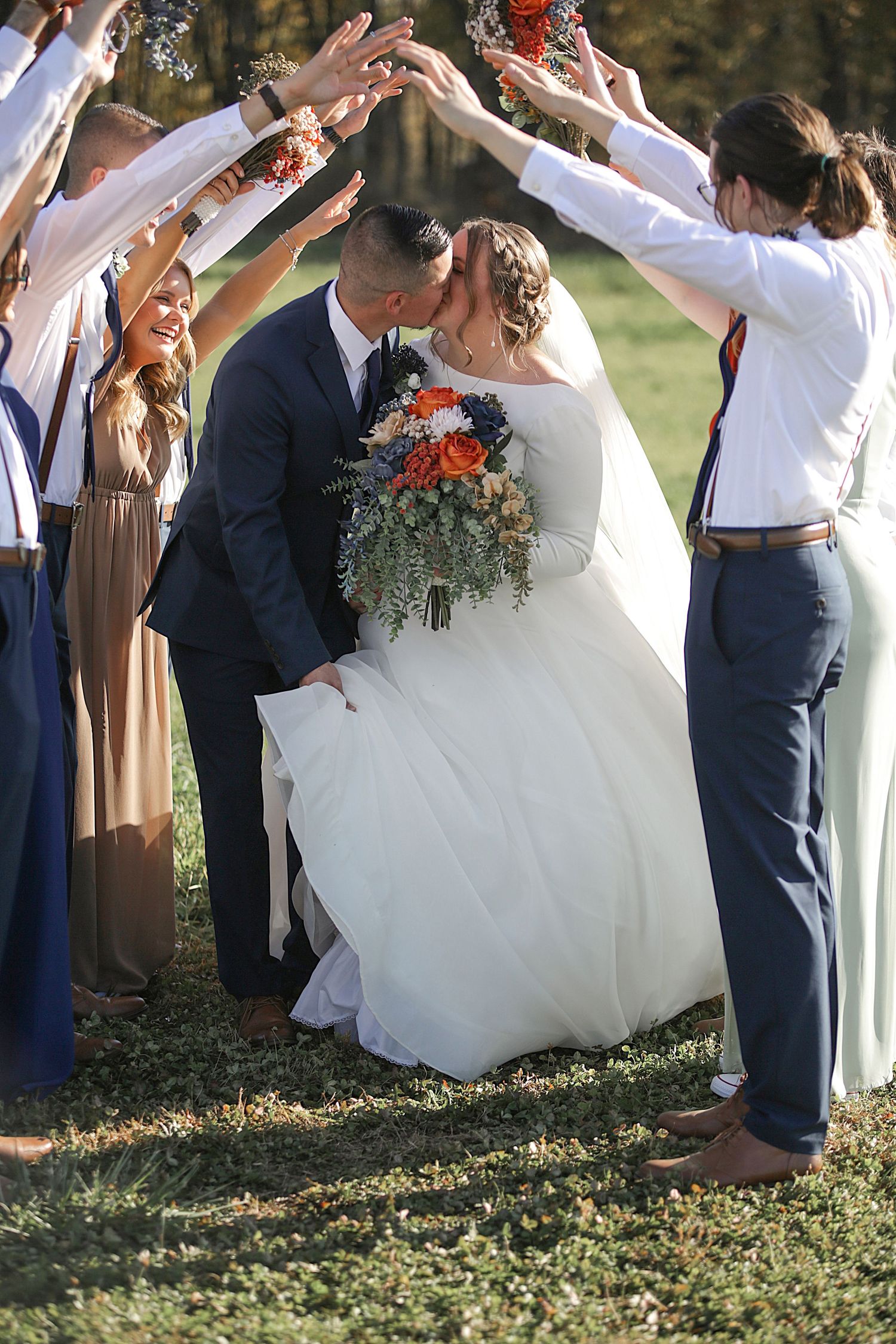 Wedding party forms traditional arch tunnel with raised arms as newlyweds share moment underneath.