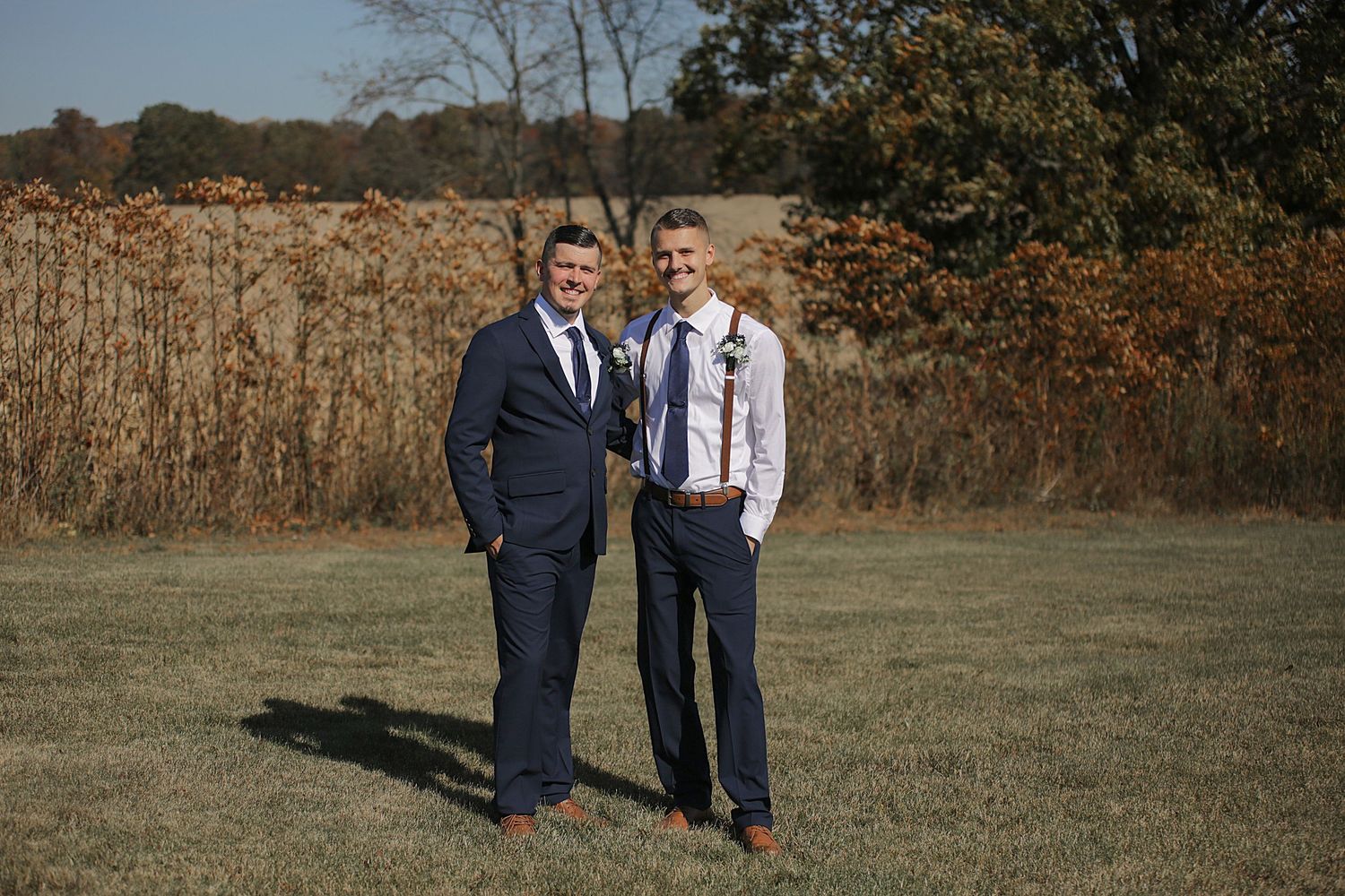 Wedding couple sharing moments on grassy field with autumn colors in background.