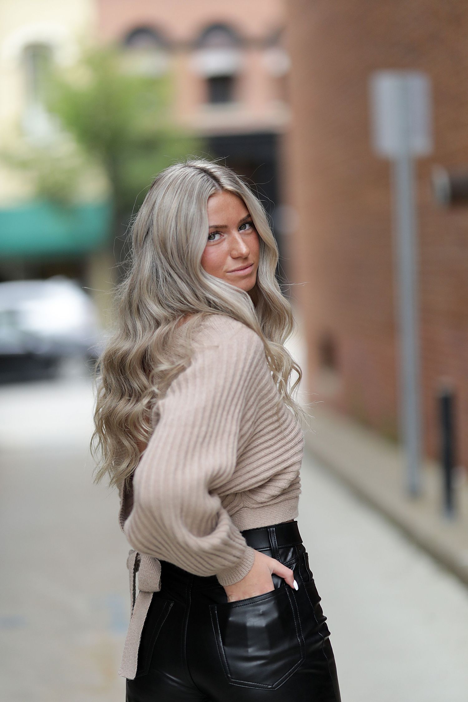 Fashionable street style outfit featuring a beige ribbed sweater and black leather pants on an urban street.