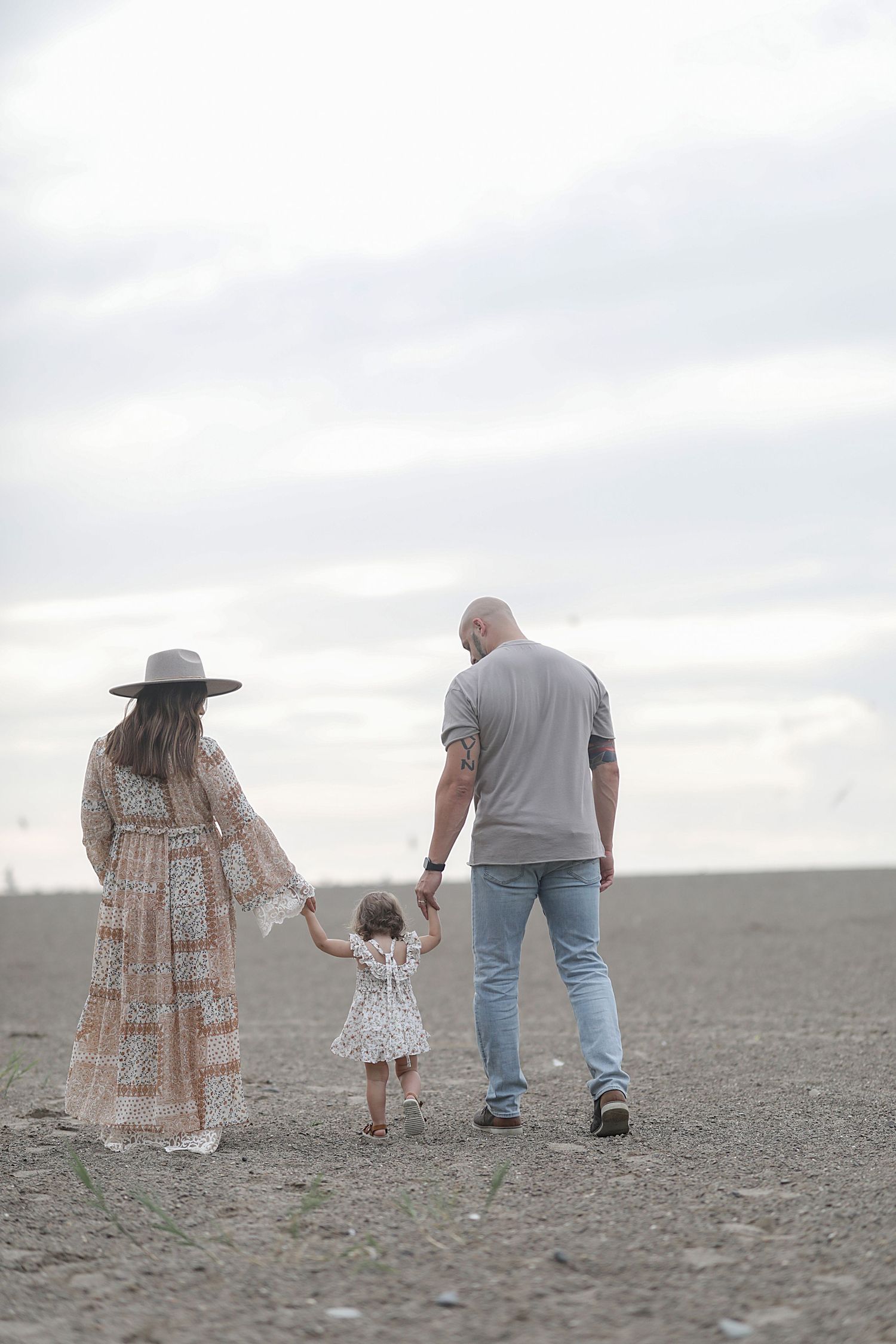 Family walks through an empty field on an overcast day, viewed from behind as they explore the barren landscape together.