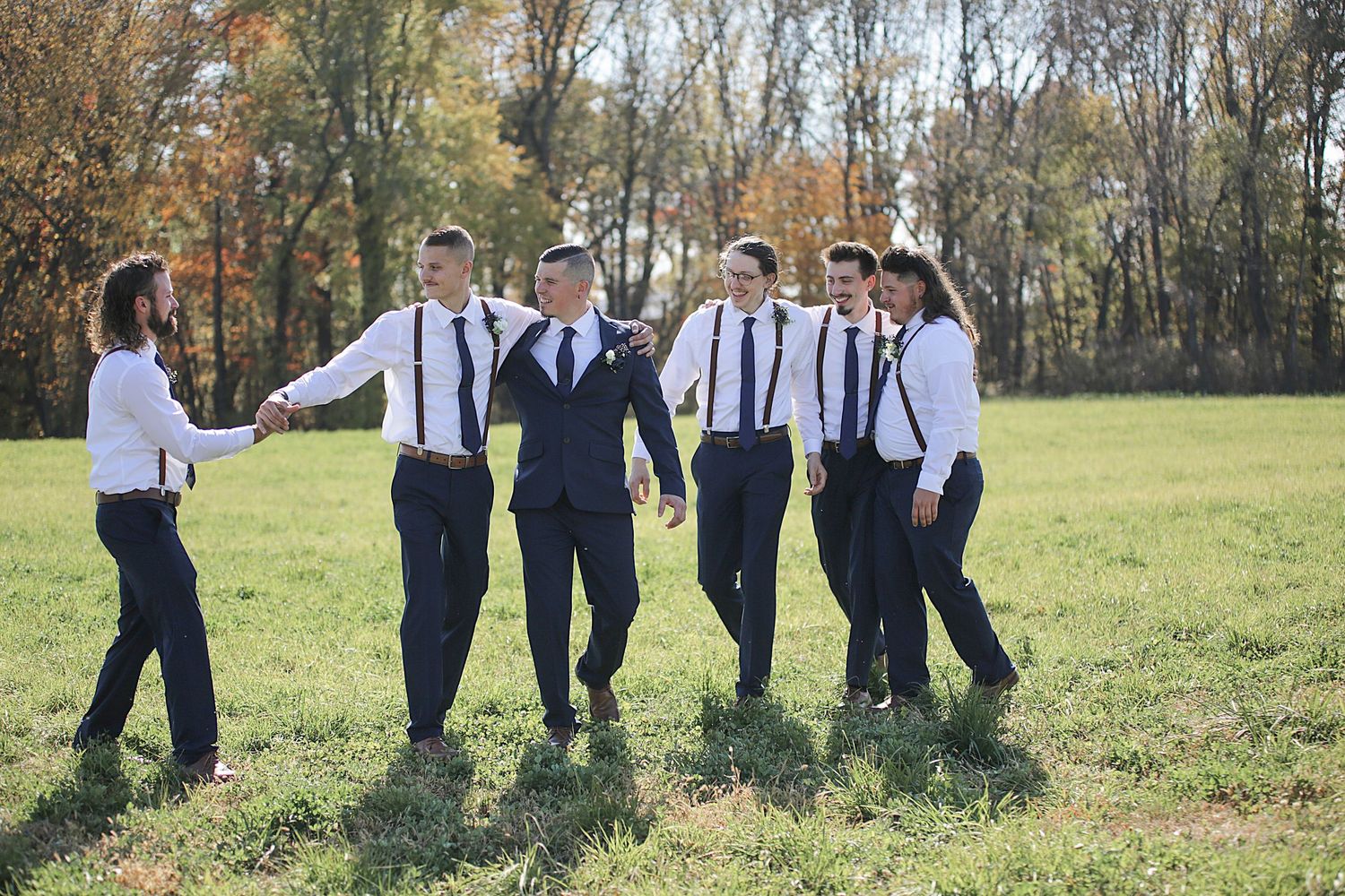 Wedding party in matching suspenders and white shirts walk through an autumn field.