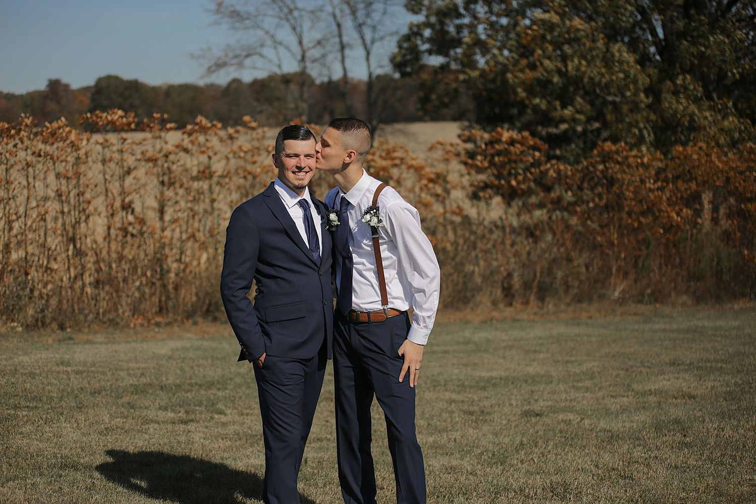 Two people share intimate moment in field during autumn wedding photoshoot.