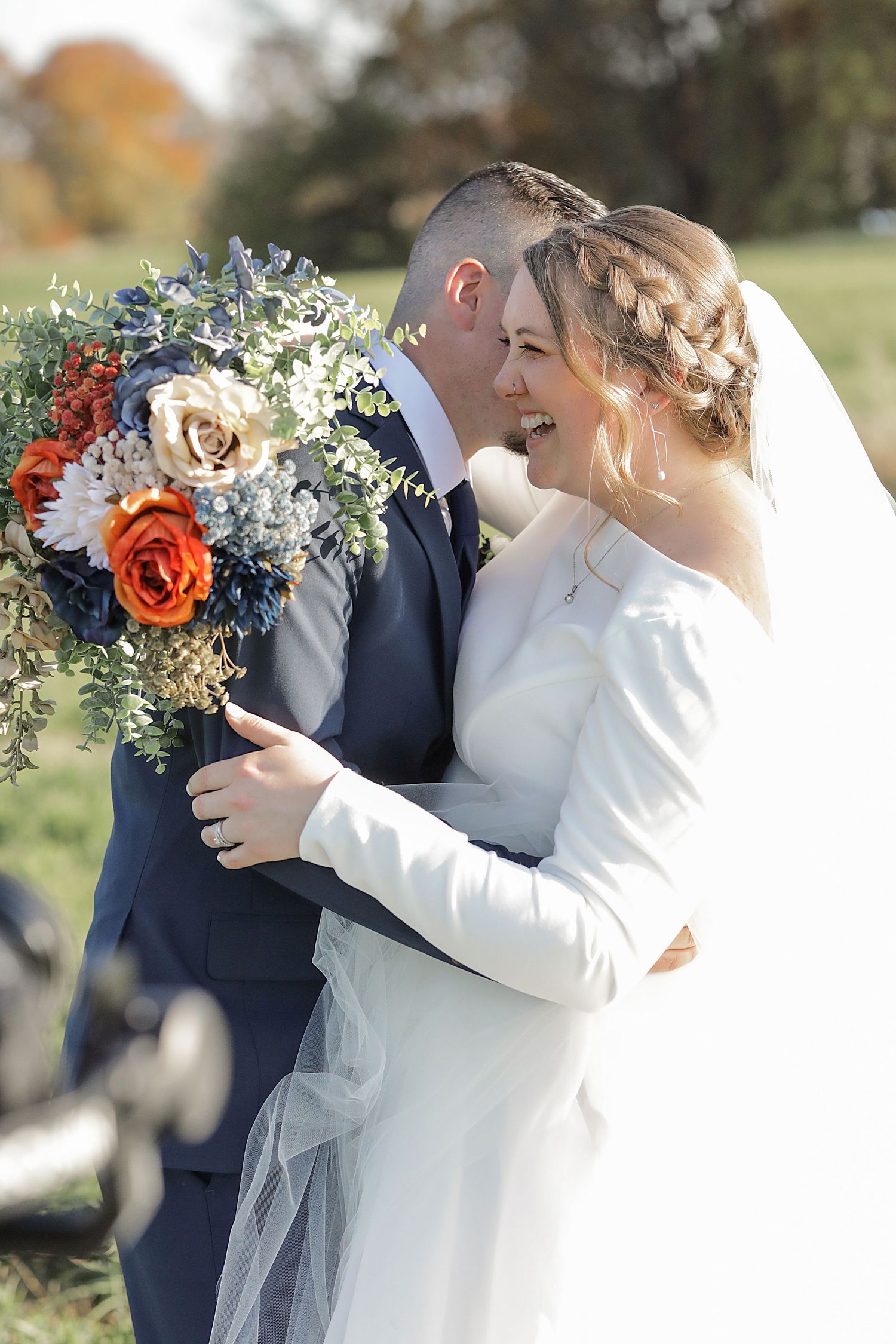 Bride holding vibrant blue and orange bouquet shares intimate moment during outdoor wedding.