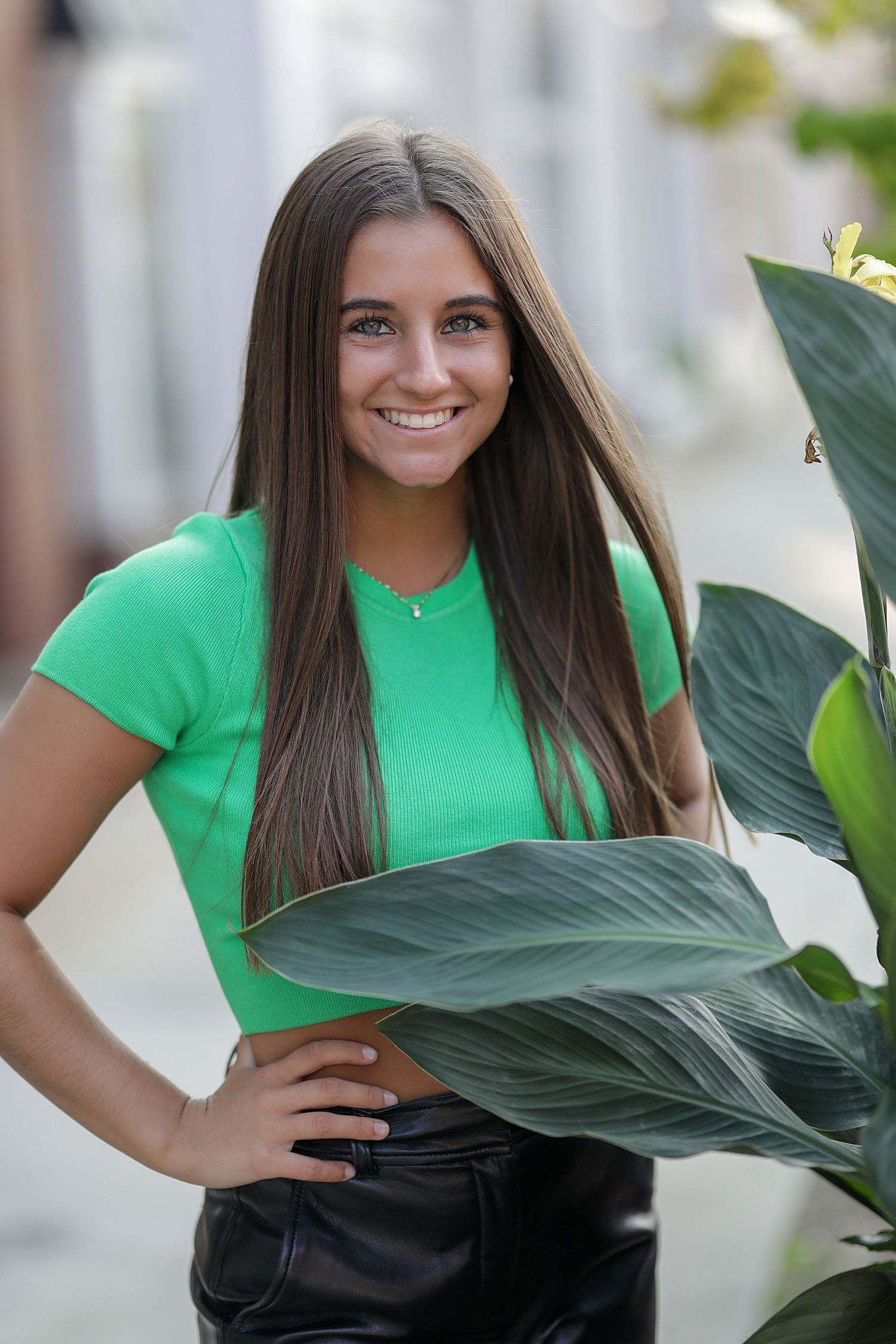 Portrait of someone wearing a bright green t-shirt and dark pants standing next to large tropical foliage.