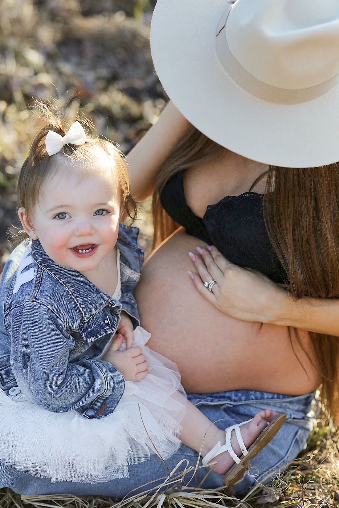 Outdoor family photoshoot with toddler in denim and white dress sitting in grassy field.