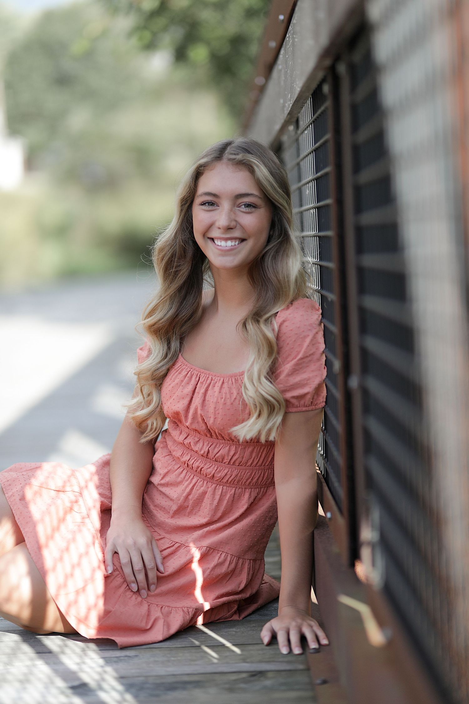 Someone wearing a coral-colored dress sits and poses casually in a series of outdoor portrait photos.