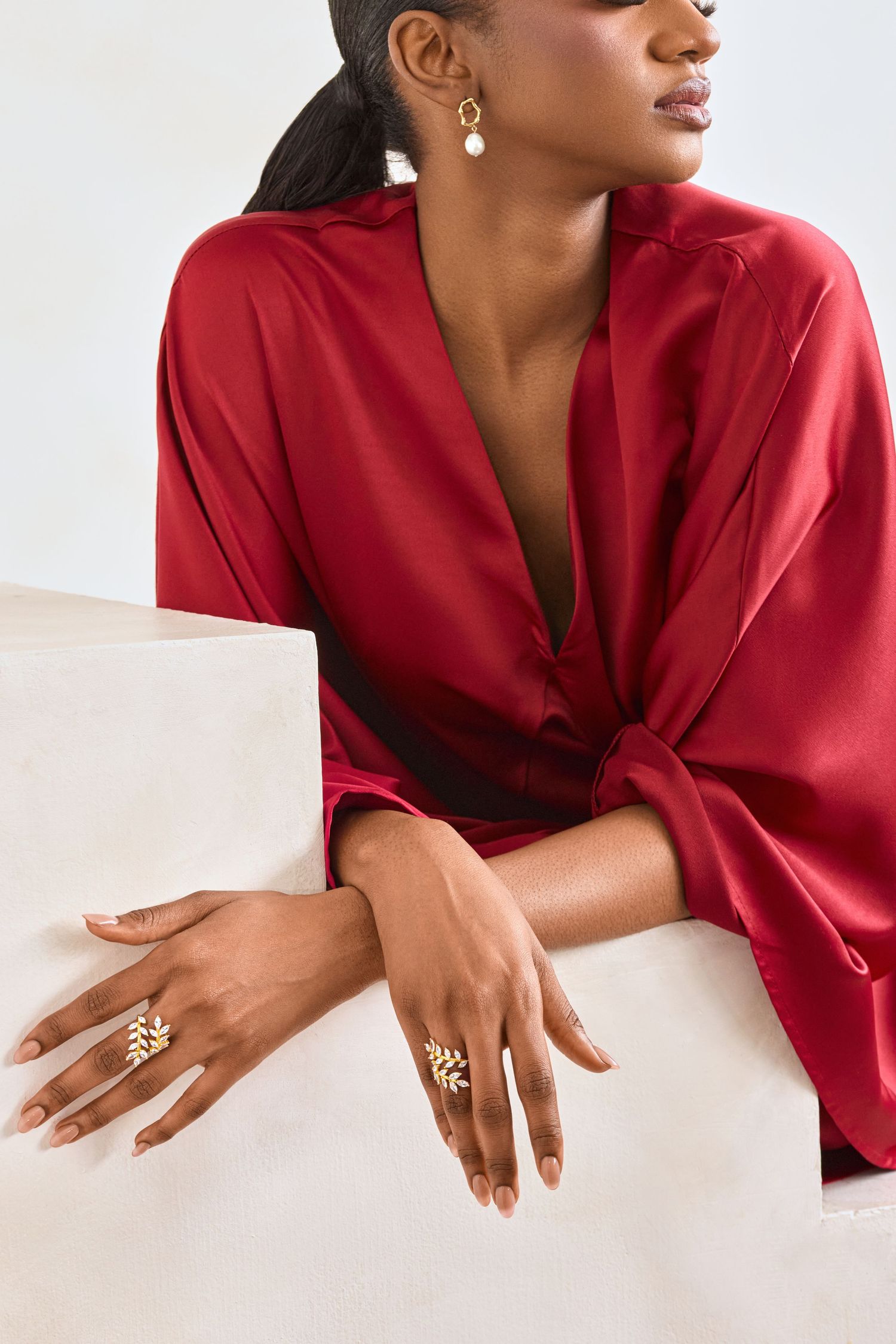 Close up of jewelry and red silk blouse on model with elegant accessories.