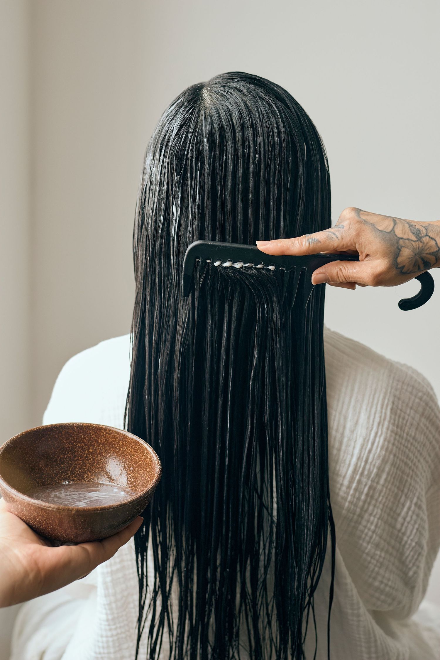 Person combing wet dark hair while holding brown bowl during hair care routine.