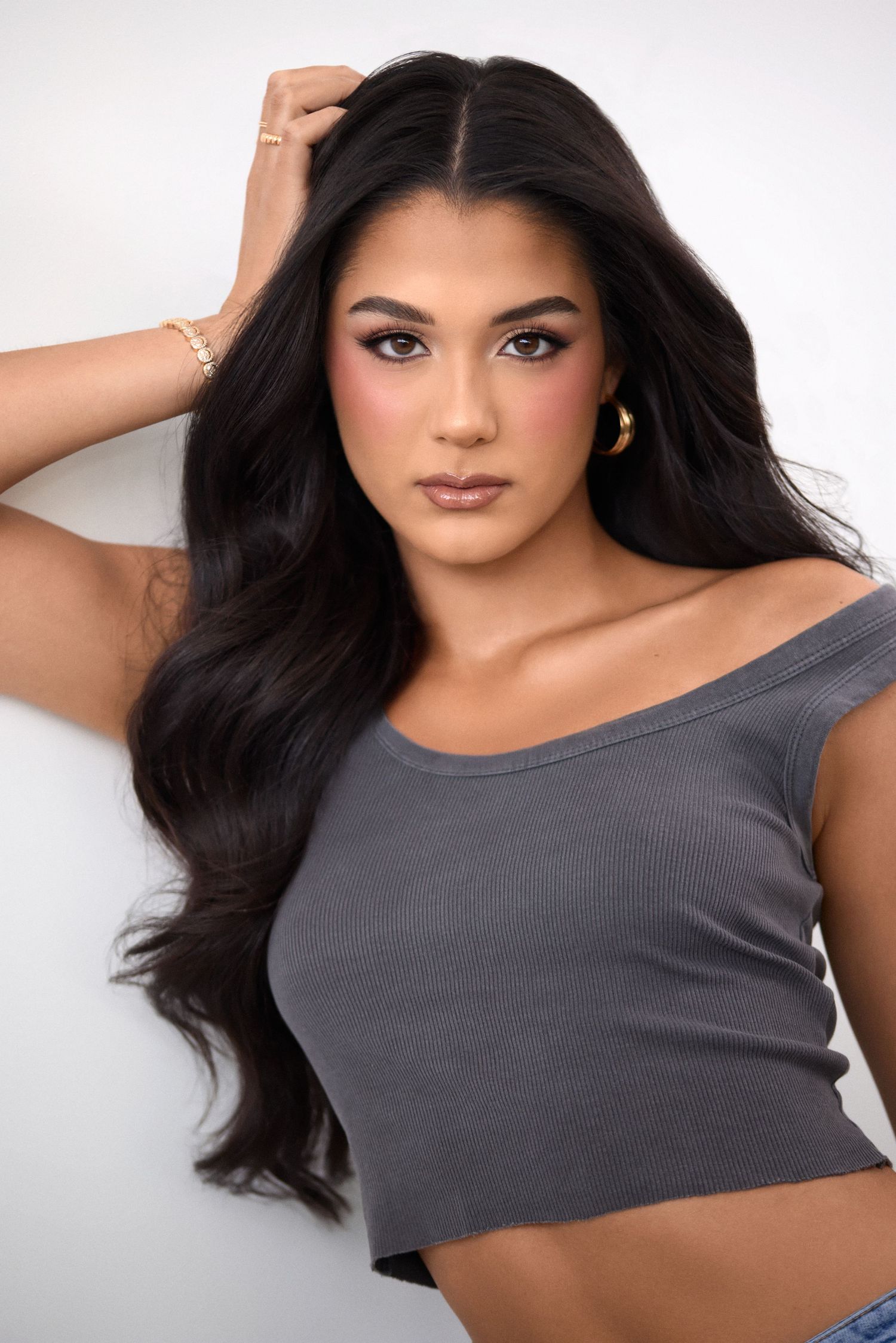 Model wearing gray crop top poses against white background with flowing dark hair and natural makeup.