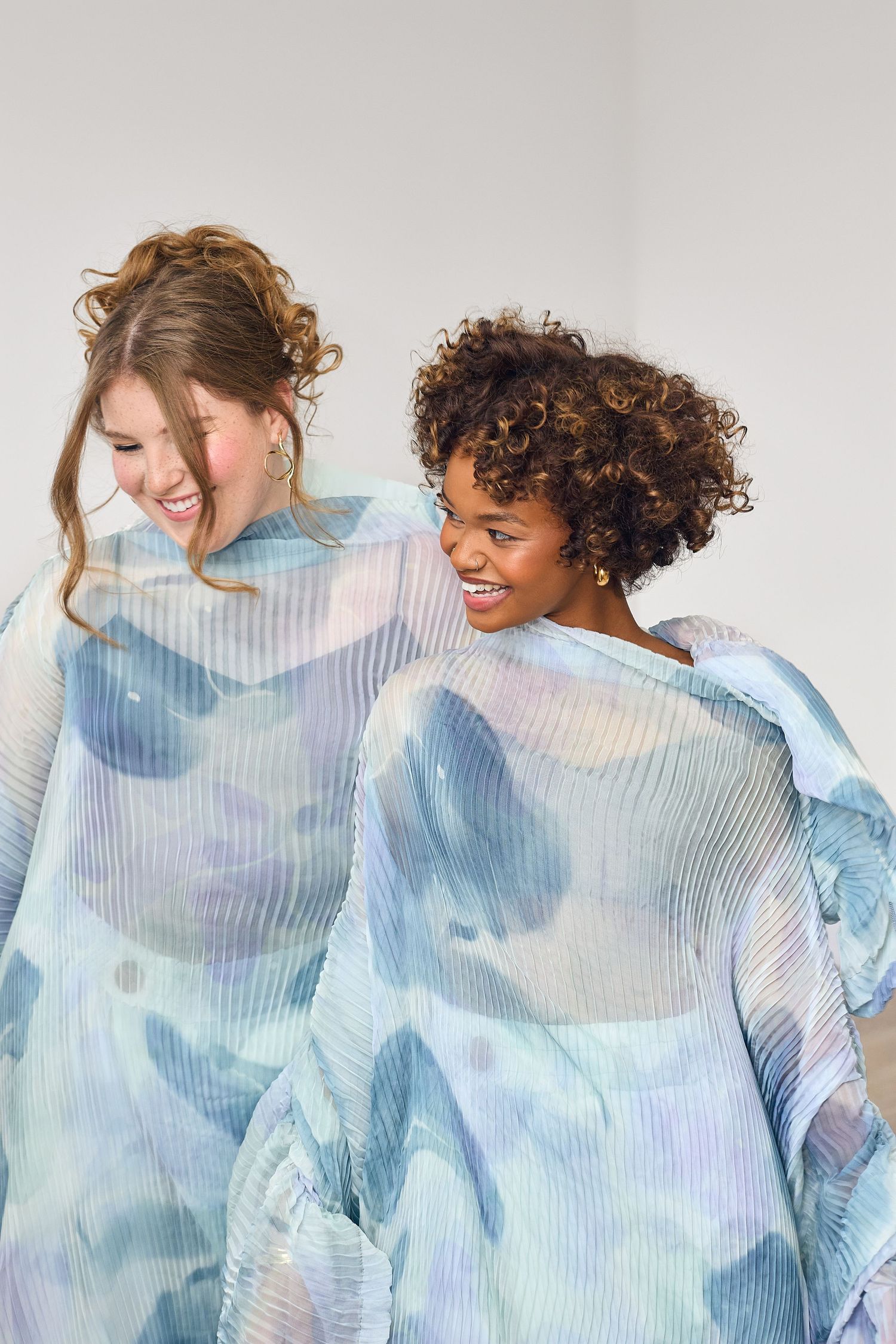 Two models wearing matching watercolor print dresses share a joyful moment together.
