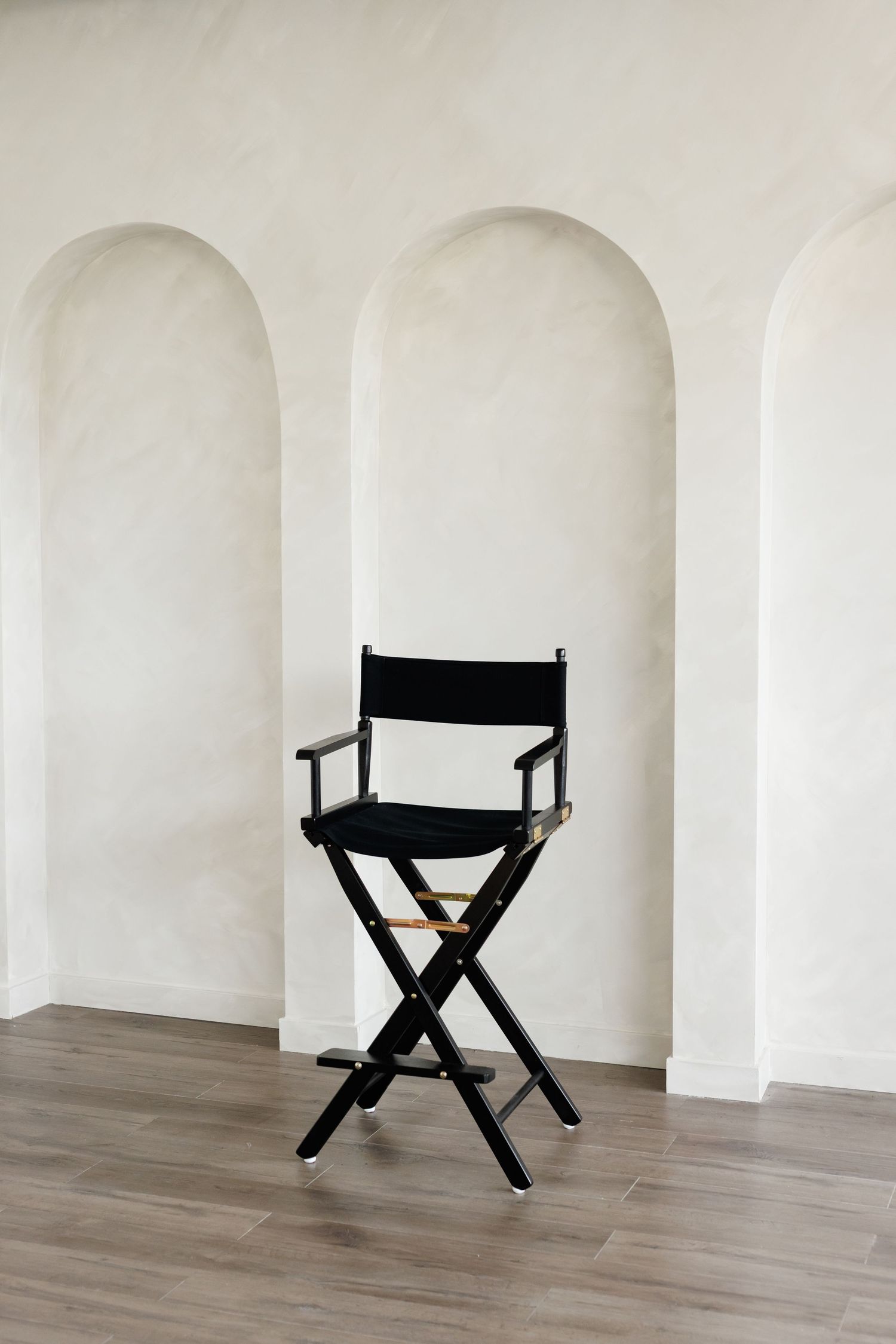 Black director's chair positioned against white wall with three arched alcoves.