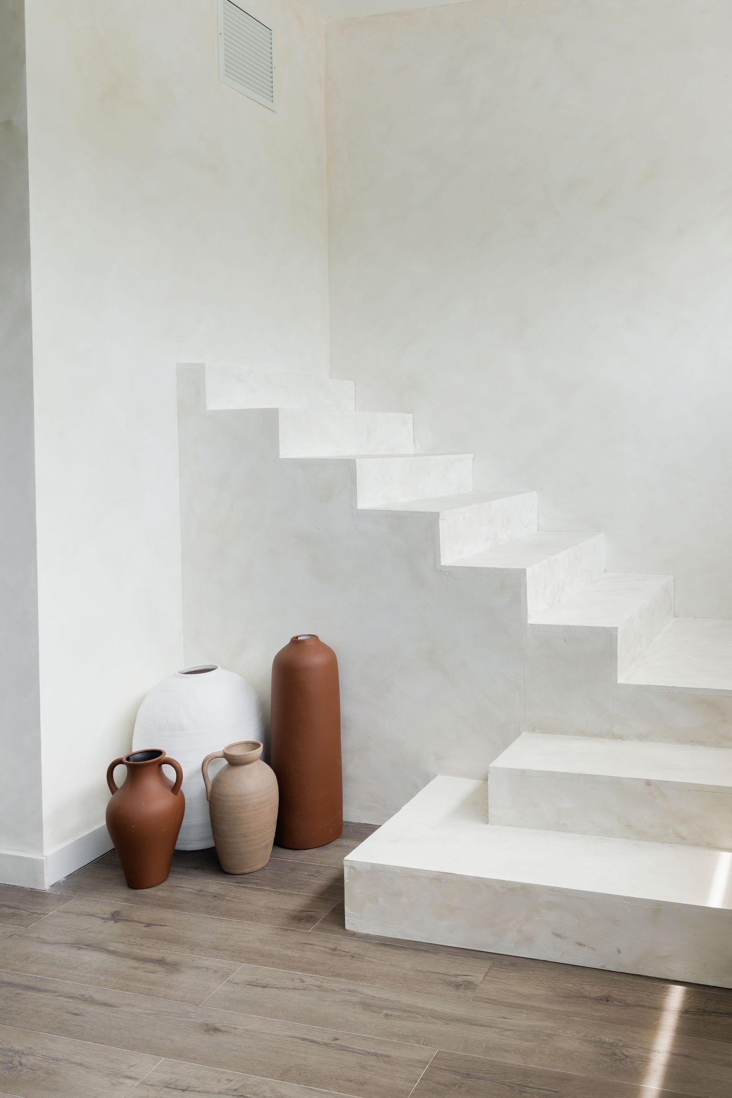 Minimalist white concrete staircase with decorative ceramic vessels beneath.