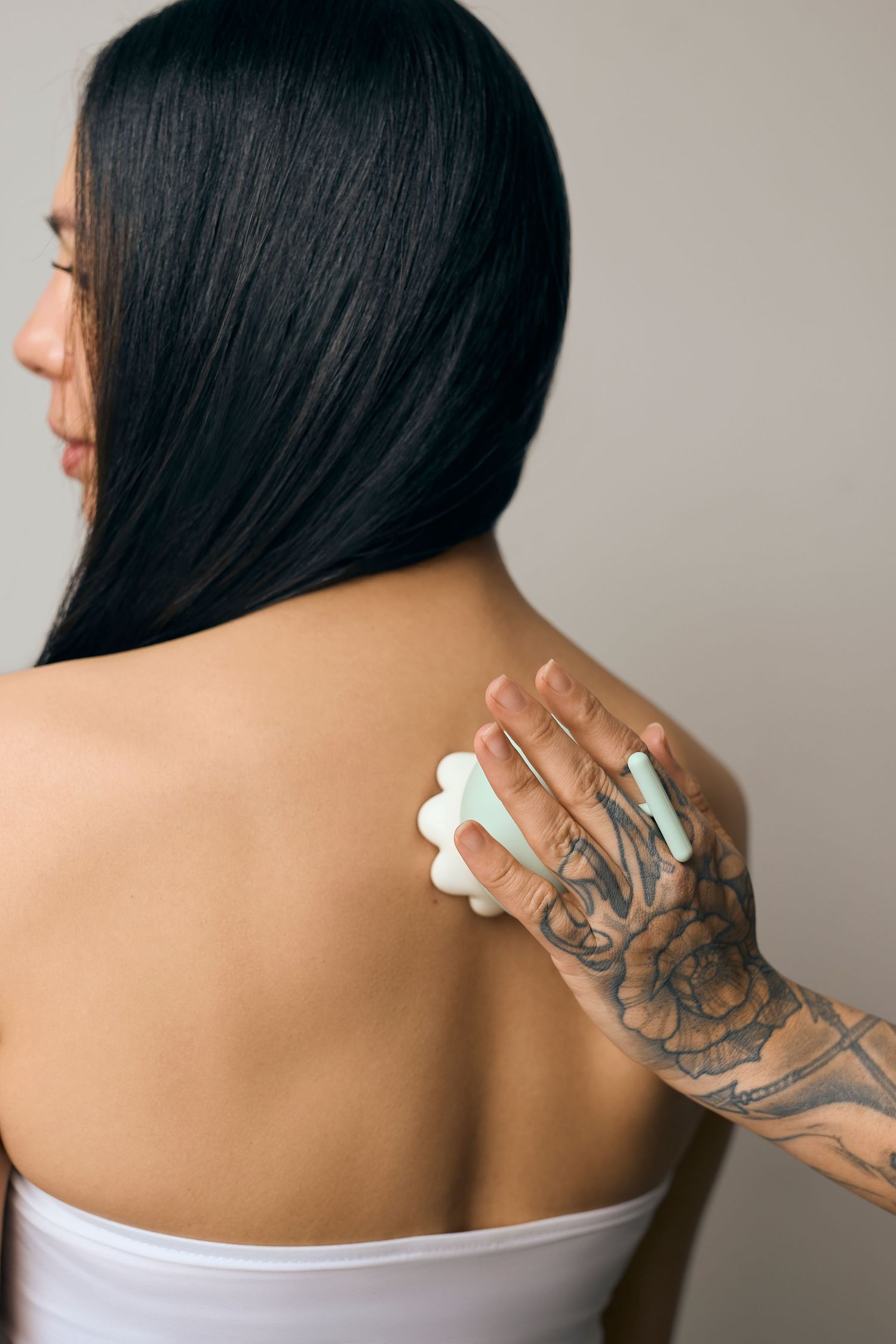 Tattooed hand holding white product against person's back wearing white top.