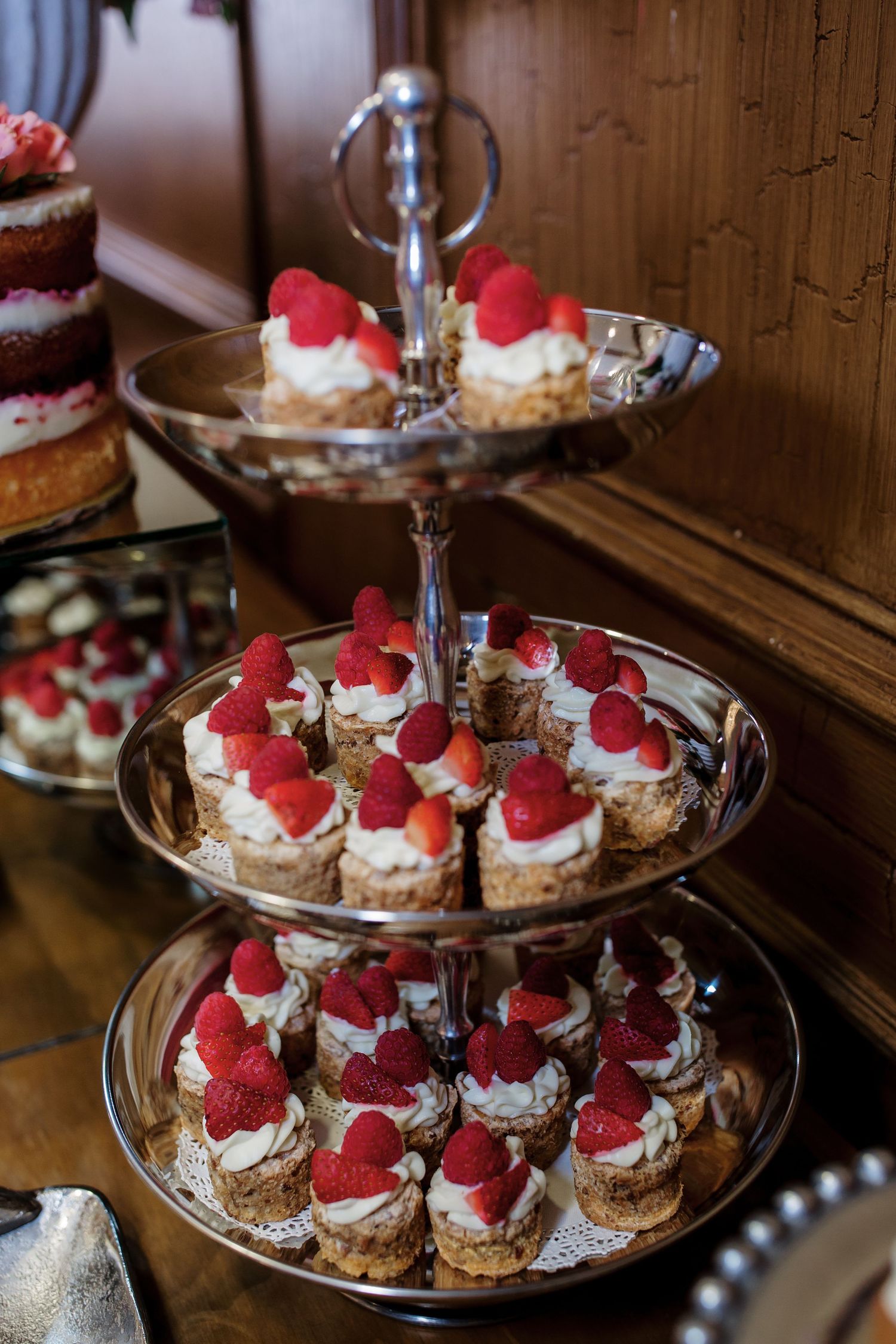 Three-tiered silver dessert stand filled with mini cream puffs topped with fresh raspberries and whipped cream.
