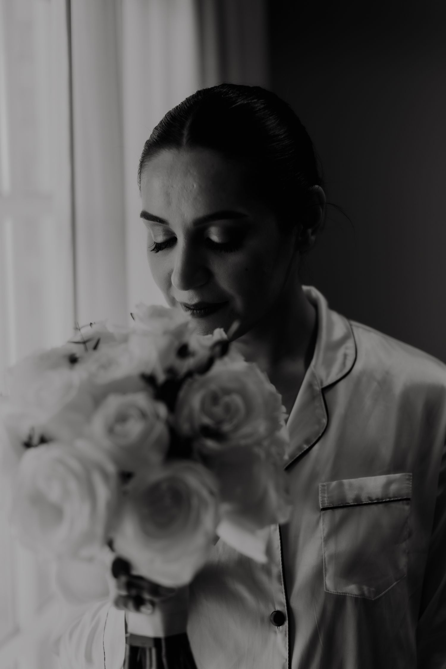 Black and white portrait with white roses in soft window light.