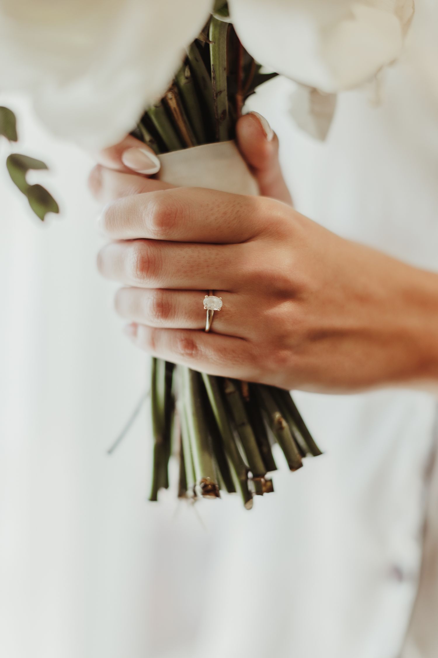 Close-up of elegant engagement ring on hand holding wrapped flower stems.