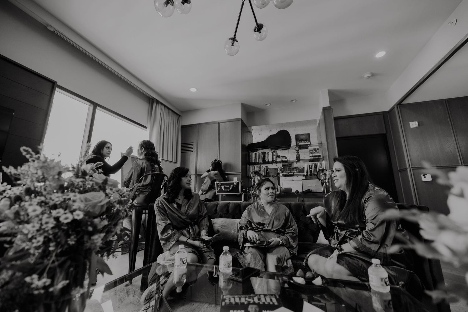 Black and white candid shot of wedding party getting ready in spacious hotel room.