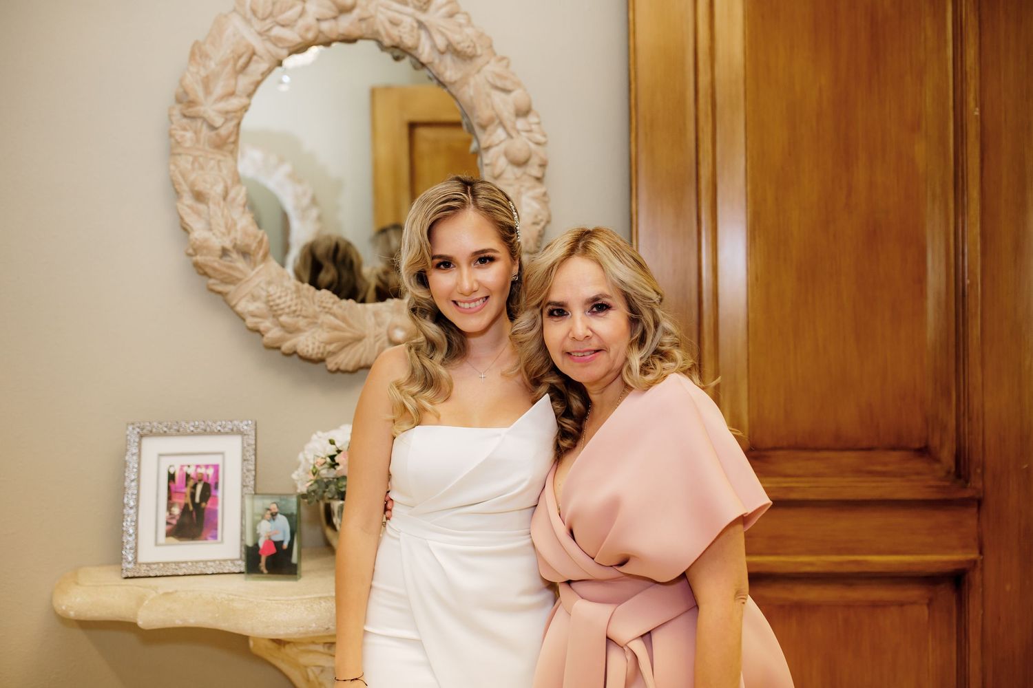 Two people posing together in an elegant room with decorative mirror and wooden panels.