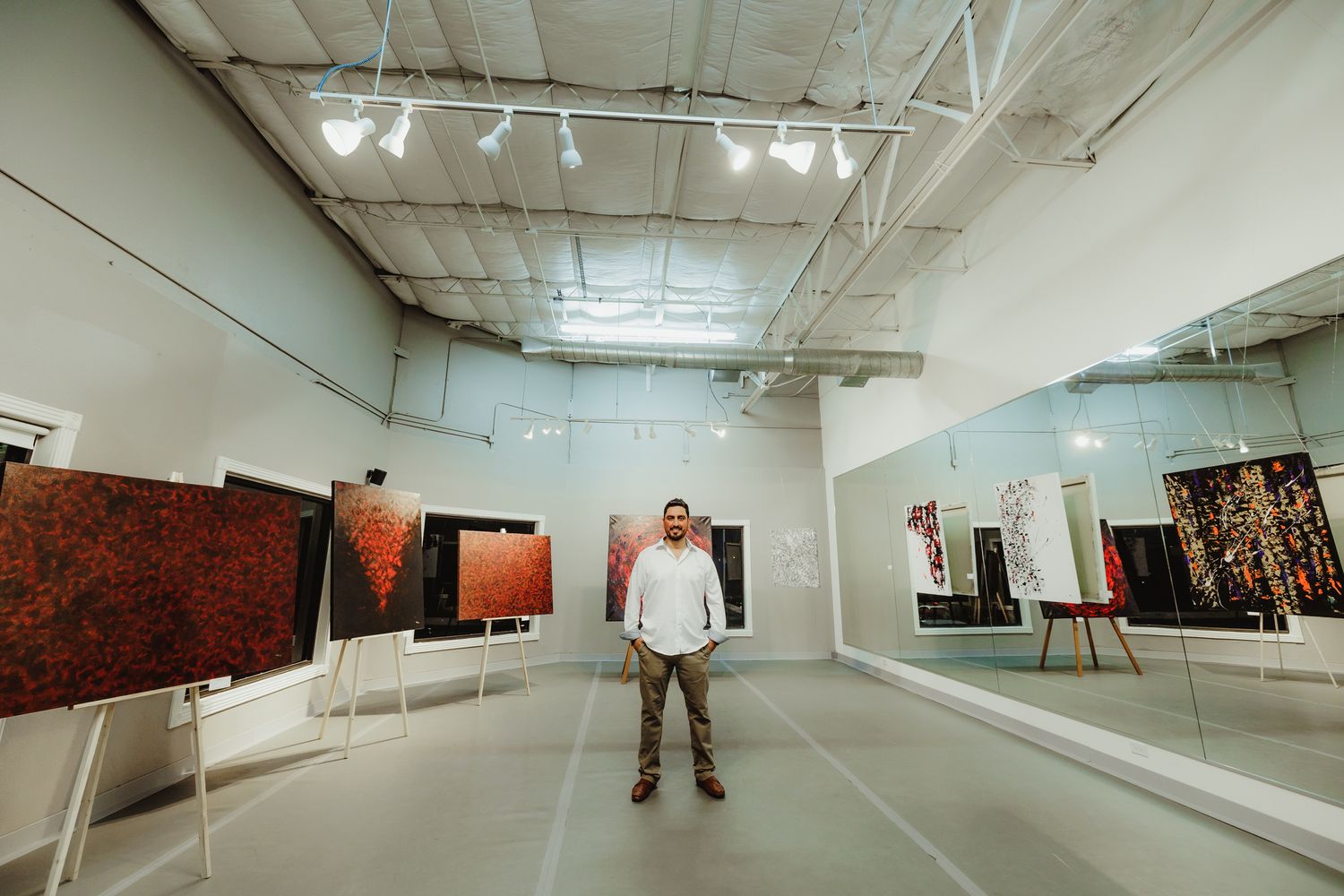 A figure stands in the center of a large gallery space with art displayed on white walls.