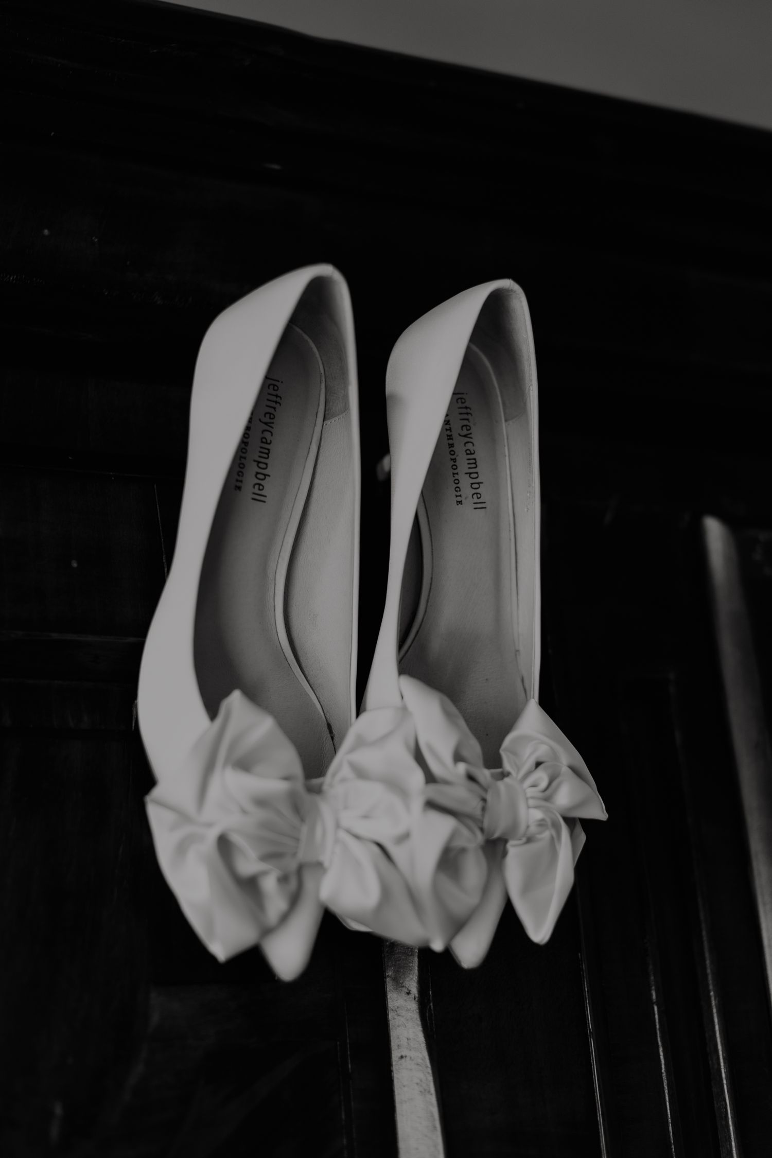 White bridal shoes with decorative bows photographed against dark background in elegant wedding detail shot.