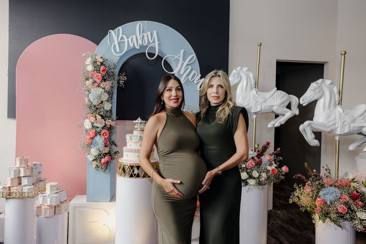 Baby shower celebration with pink arch backdrop decorated with floral arrangements and white fabric draping.