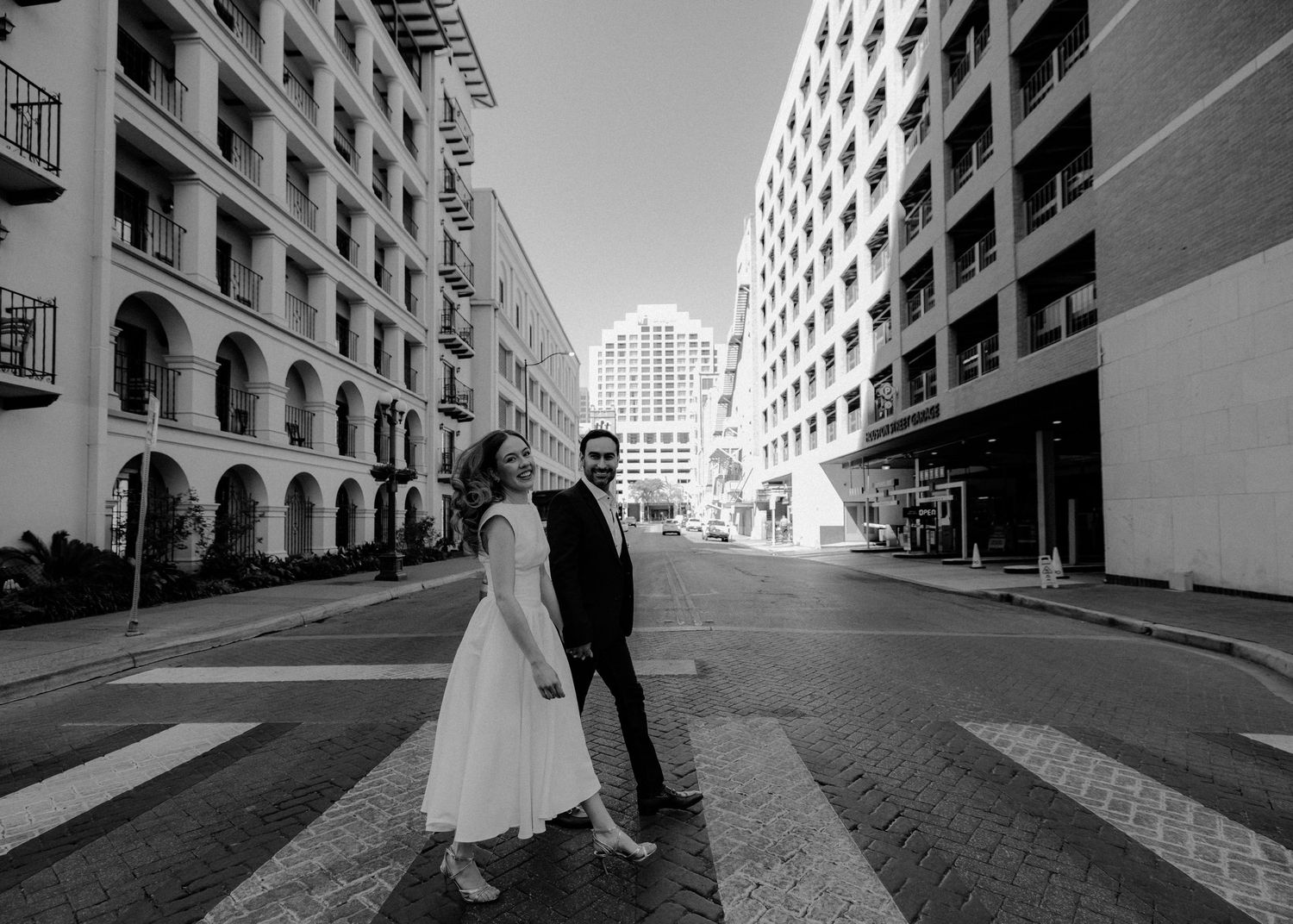 Black and white photo of a couple standing in the middle of an urban street with tall buildings.