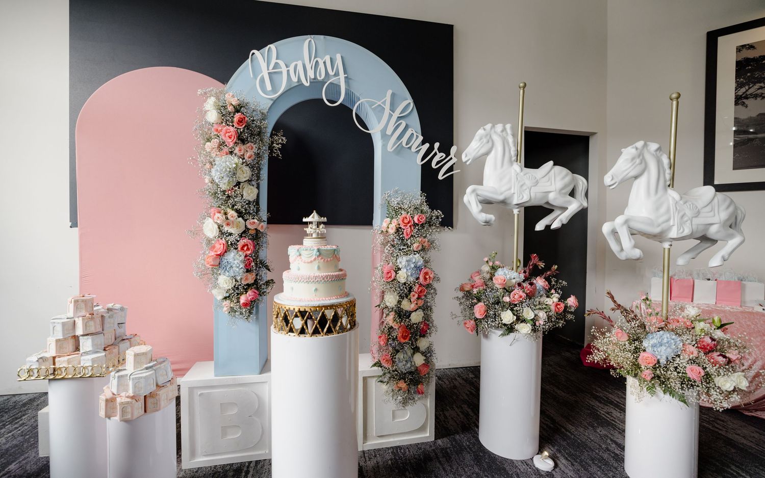 Pink and blue wedding decor setup with floral arches, white pedestals, and shiny balloon accents for a gender reveal party theme.