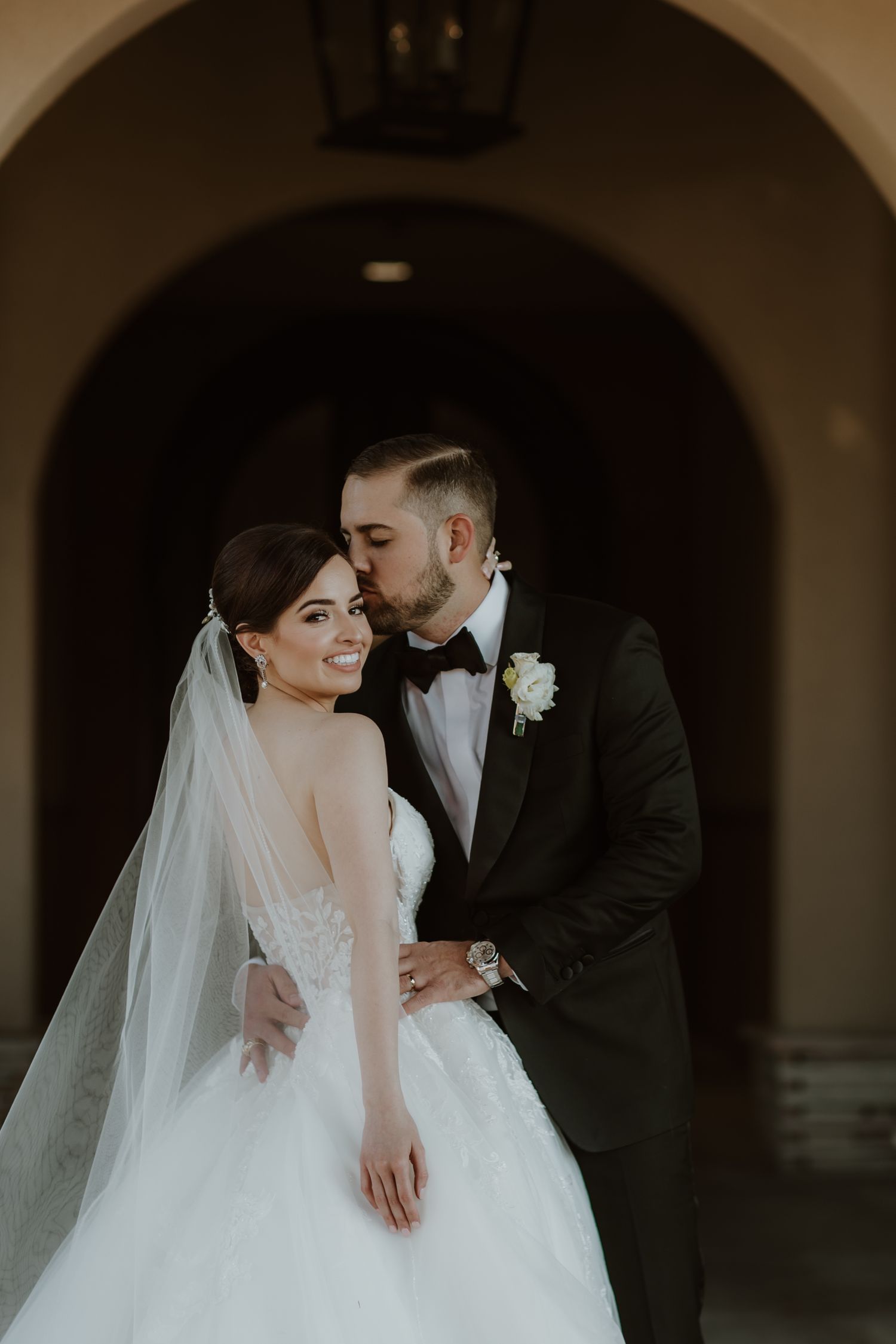 Romantic wedding portrait under arched doorway with moody lighting.