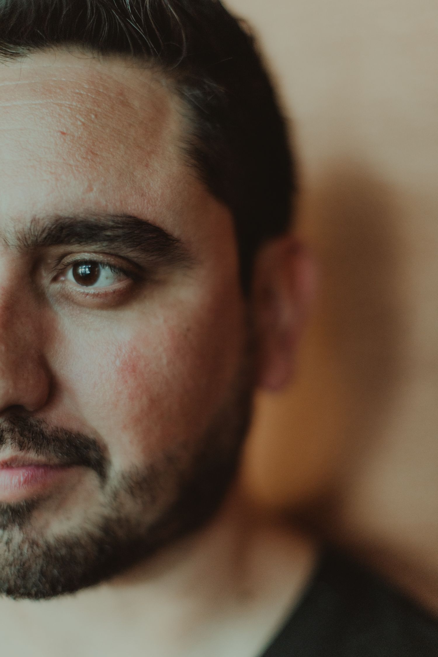 Close up portrait showing half of a bearded face with intense eyes in warm lighting.
