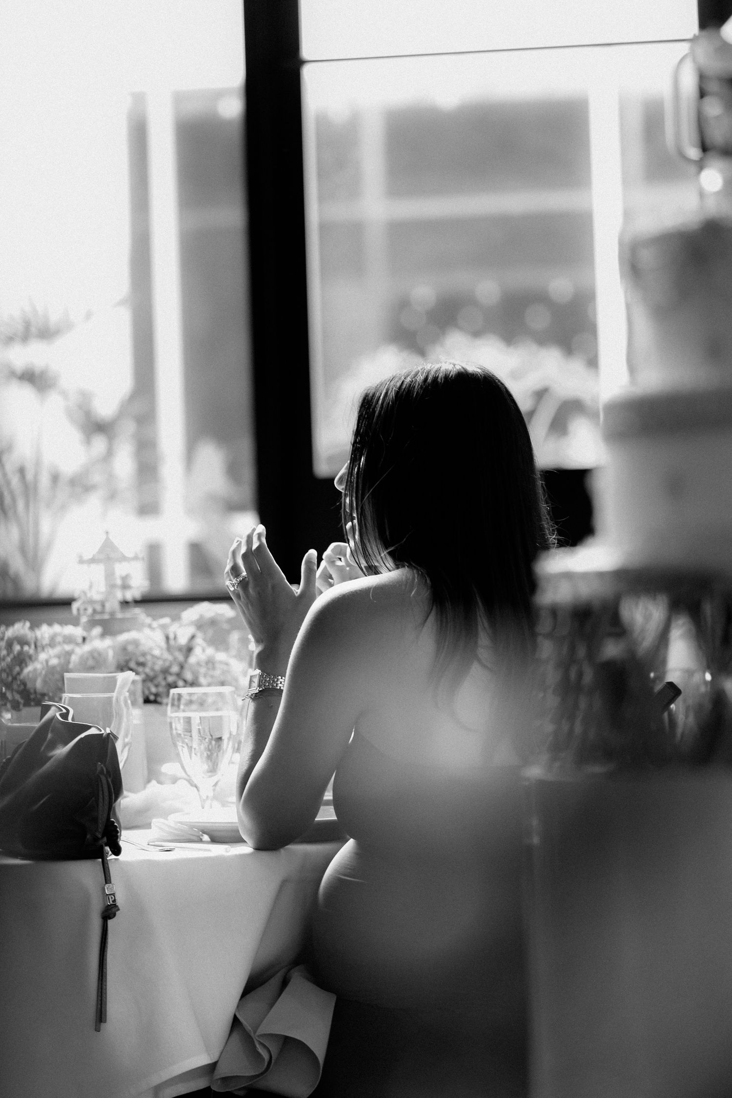 A silhouetted figure sits alone at a restaurant table by a window in black and white moody lighting.